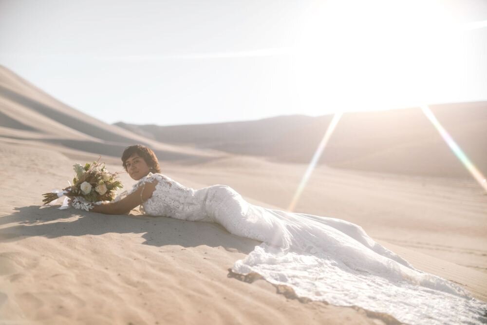 Bride laying in sand dunes wearing Randy Fenoli wedding gown holding bridal bouquet