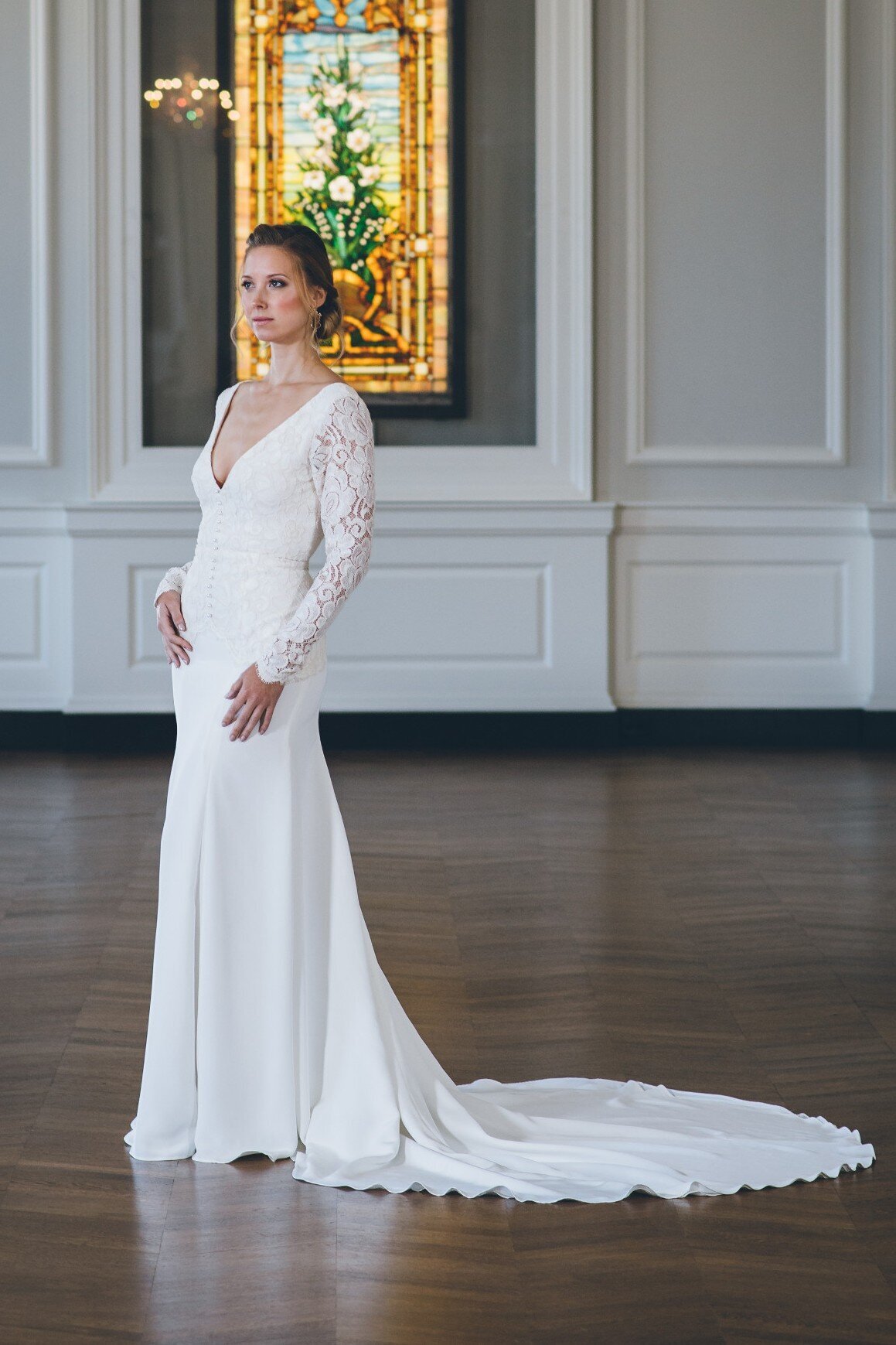 Bibi is a crepe and lace wedding dress in a fit-and-flare silhouette with a v-neck, long sleeves, and long train.