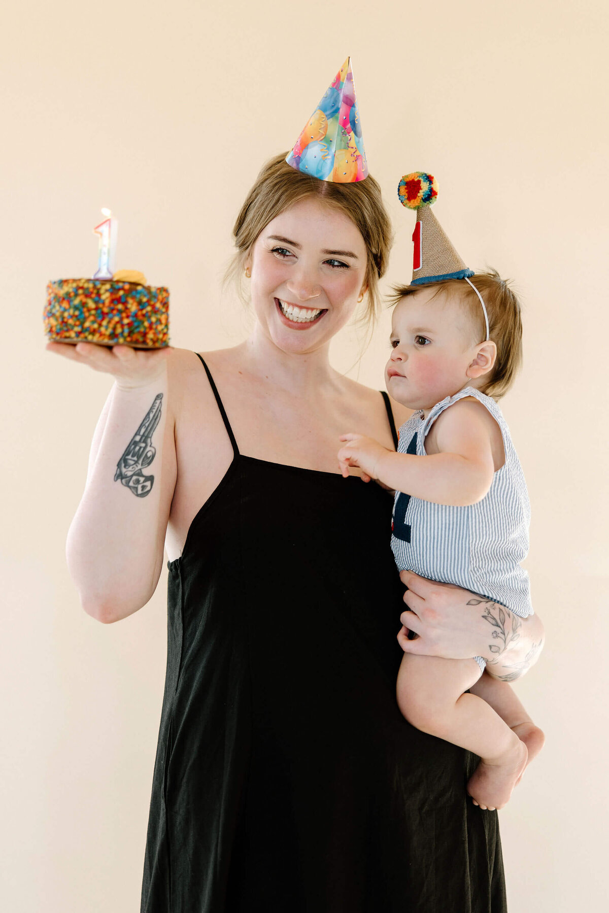 Milestone baby pictures of baby boy and mom on 1st birthday wearing party hats and mom holding birthday cake