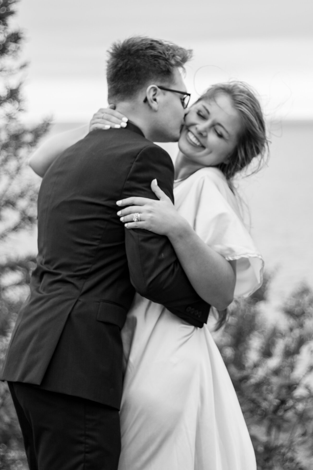 After an elopement, the groom kisses the brides cheek as she beams with joy towards the Duluth wedding photographer, S Jacobson Photography, on the shore of Lake Superior.