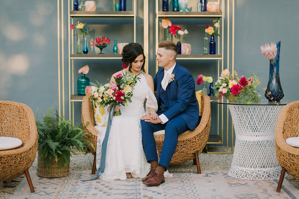 Bride and groom sit together with bouquet in brightly colored boho wedding reception