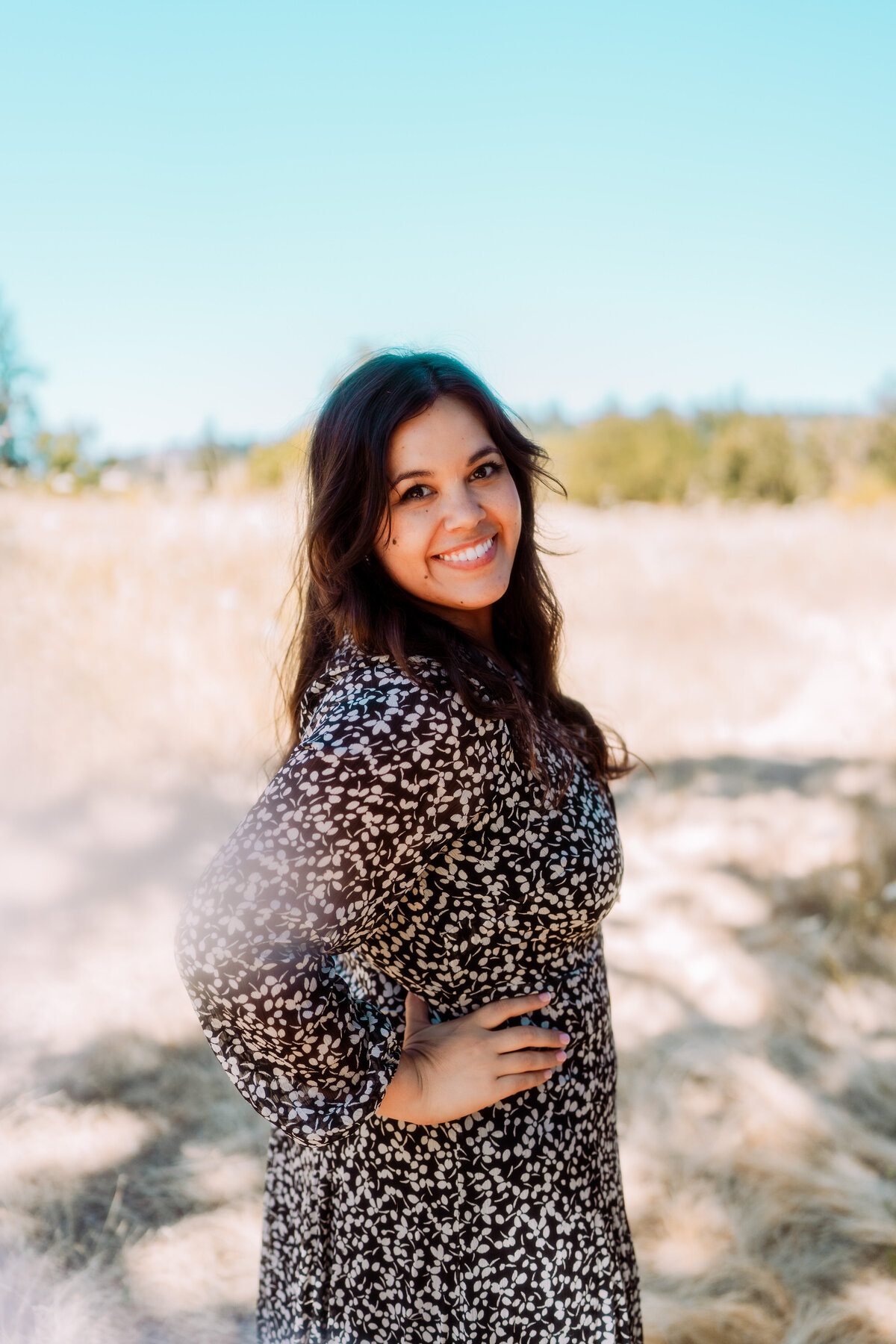 Woman smiling in a patterned dress in a sunlit field – natural light branding portrait by Mewphotovideo