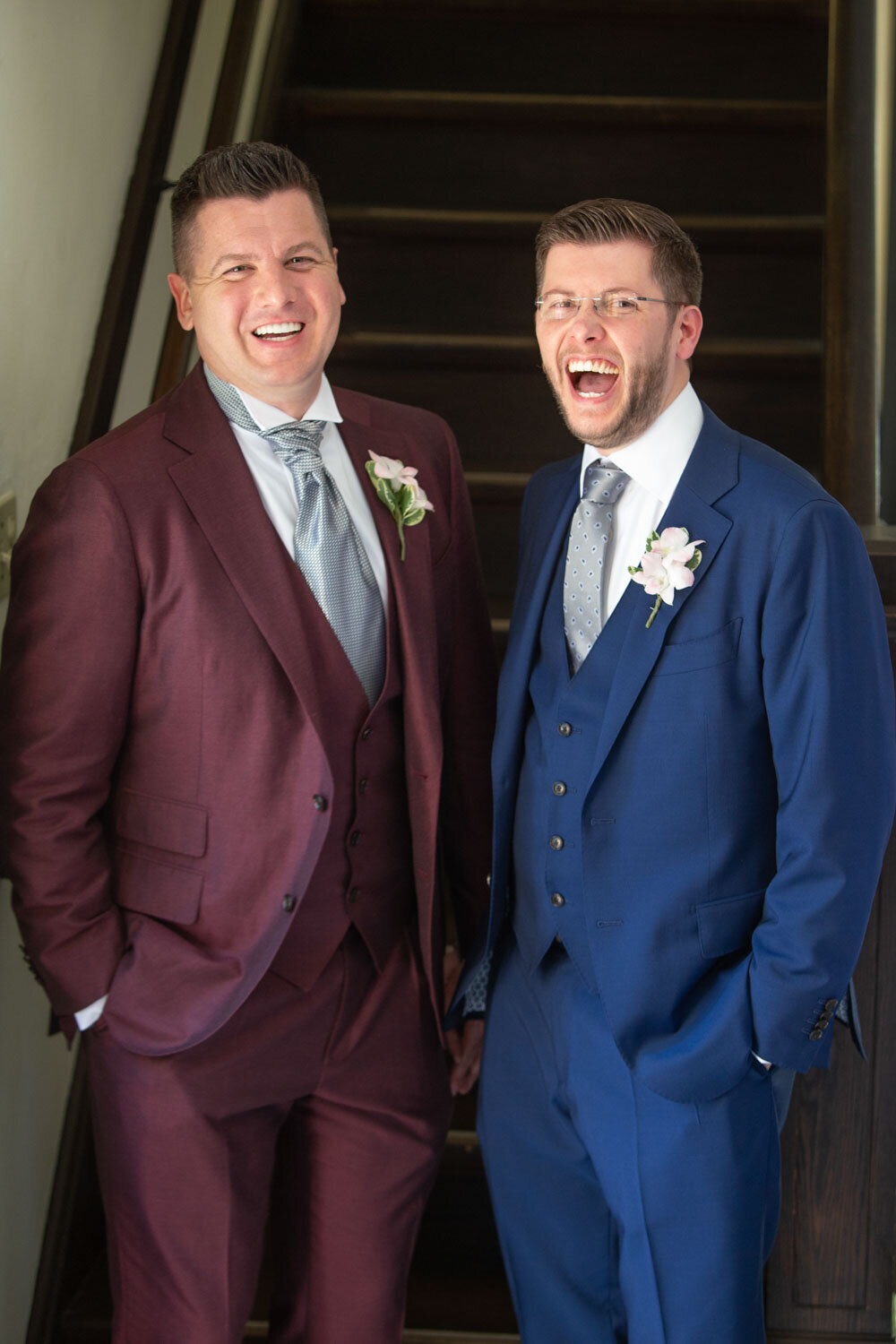 Groom and groom in suits are standing next to each other and smiling
