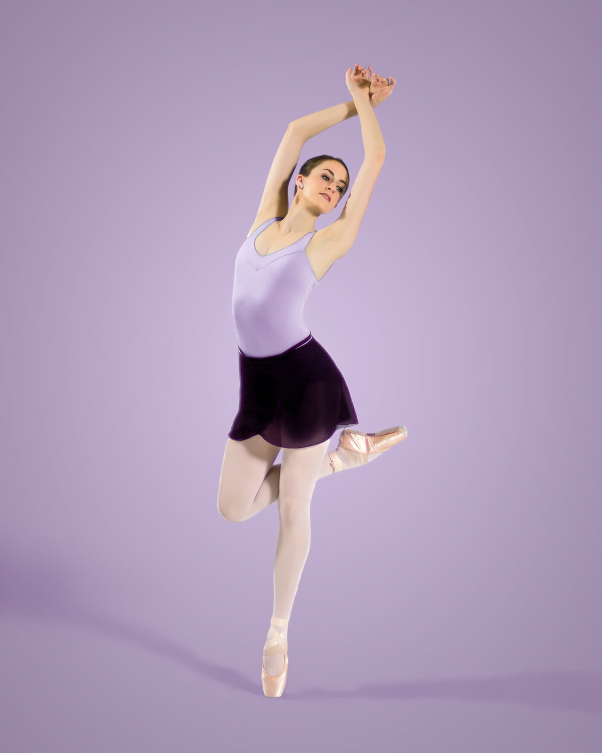 Stunning Ballerina in a purple Leotard and dance skirt posing en pointe on a purple backdrop