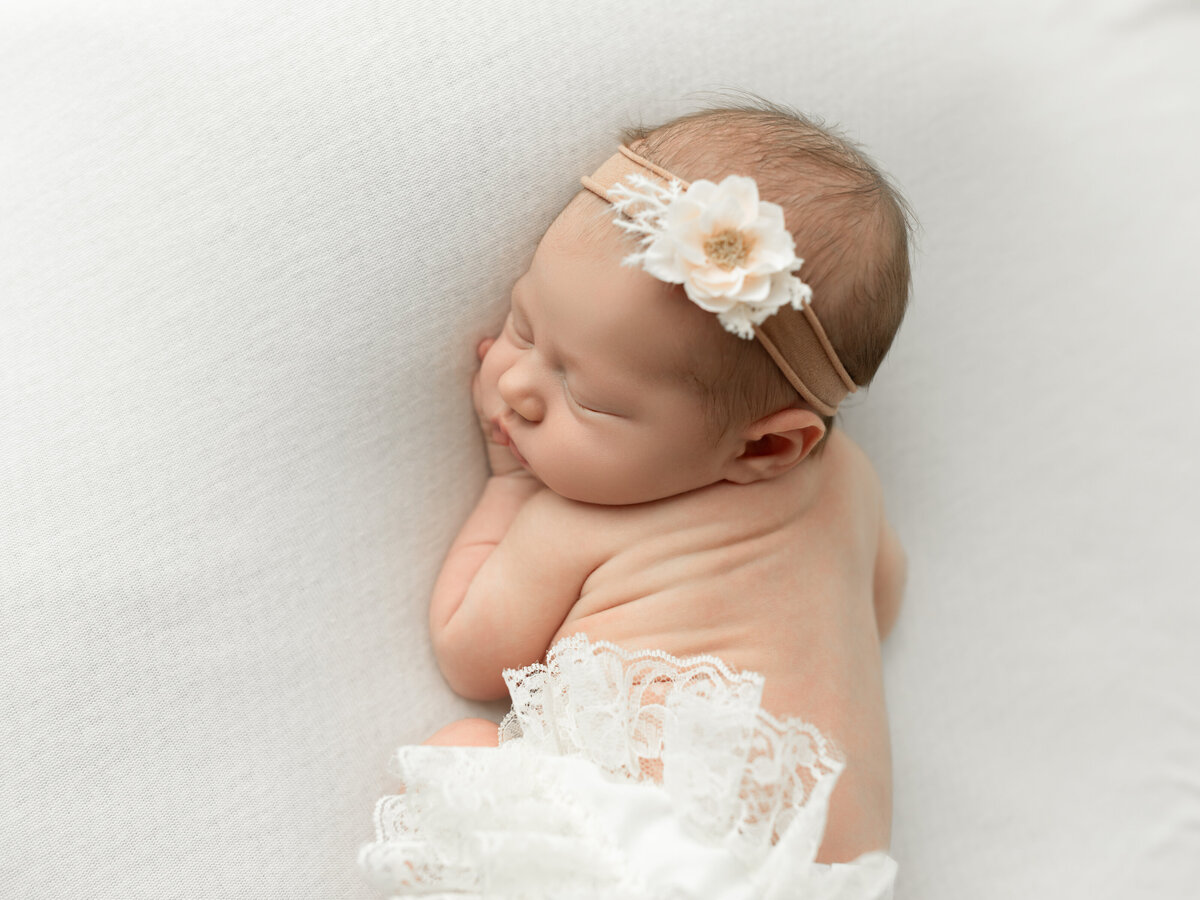 newborn baby boy in white hat posed on white fabric for studio portraits cleveland newborn photographer