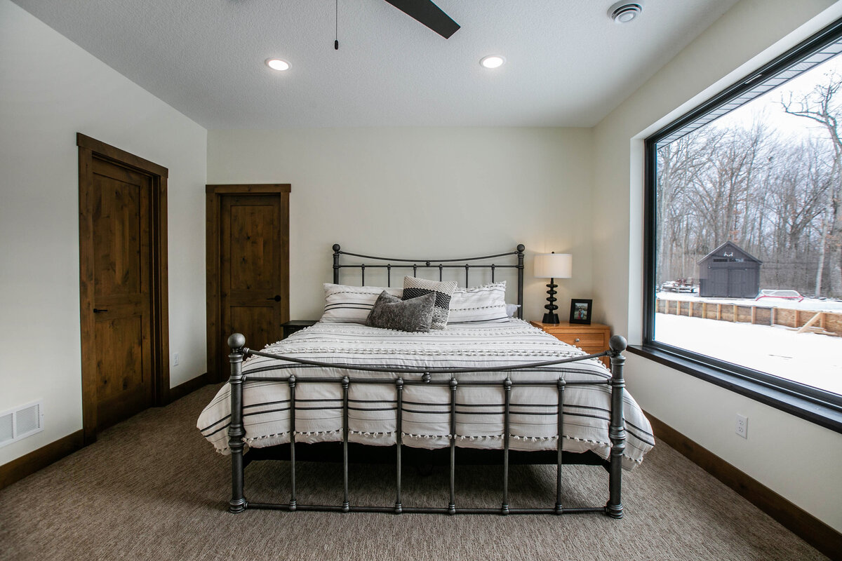 Spacious primary bedroom in custom Otsego home with natural light and dark wood accents
