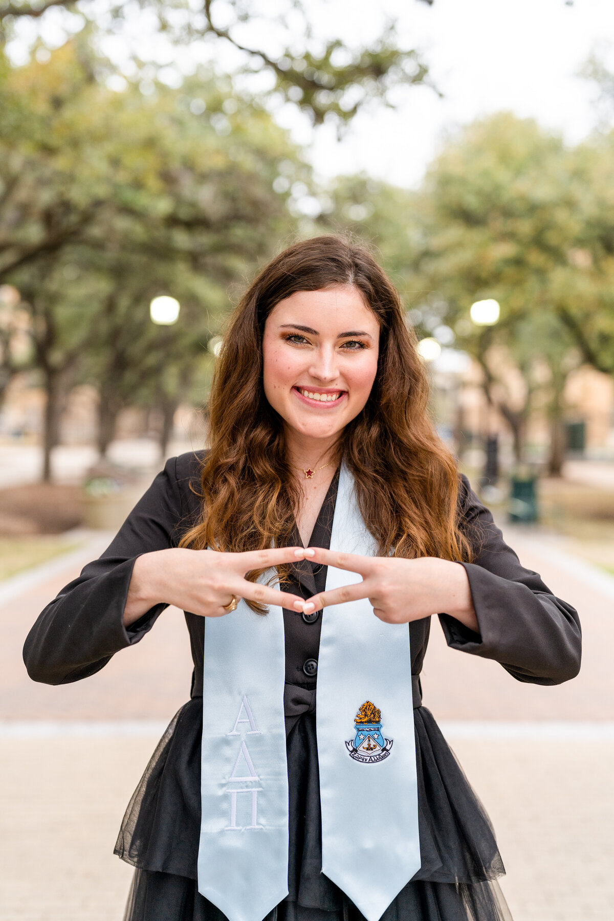 Texas A&M senior girl smiling and showing Pi Phi sign while wearing sorority stole and black dress in Military Plaza