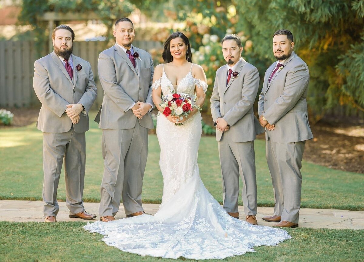 Bride stands with groomsmen at Venue 92 in the side garden. 