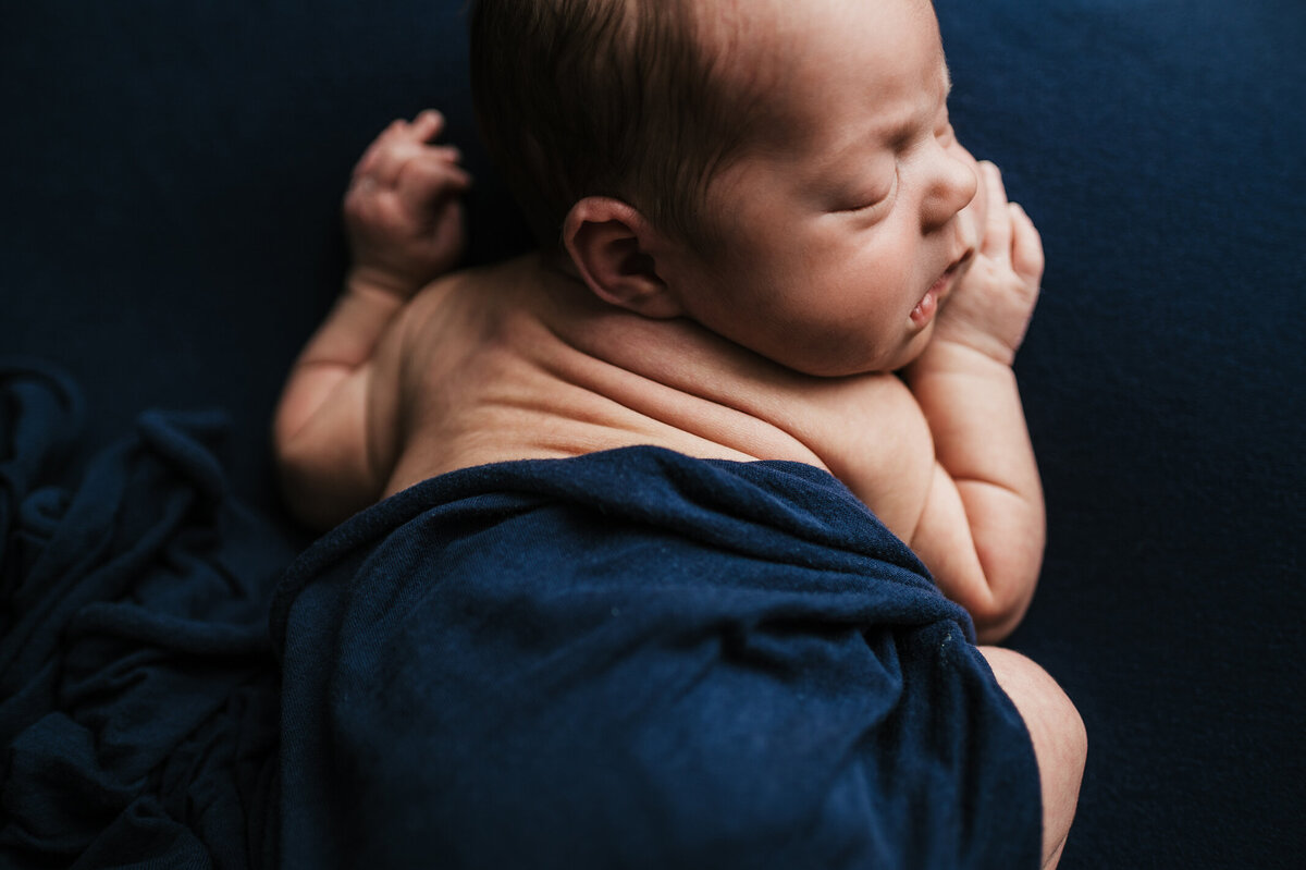 Sleeping baby laying on a blue background  with scrunched back rolls