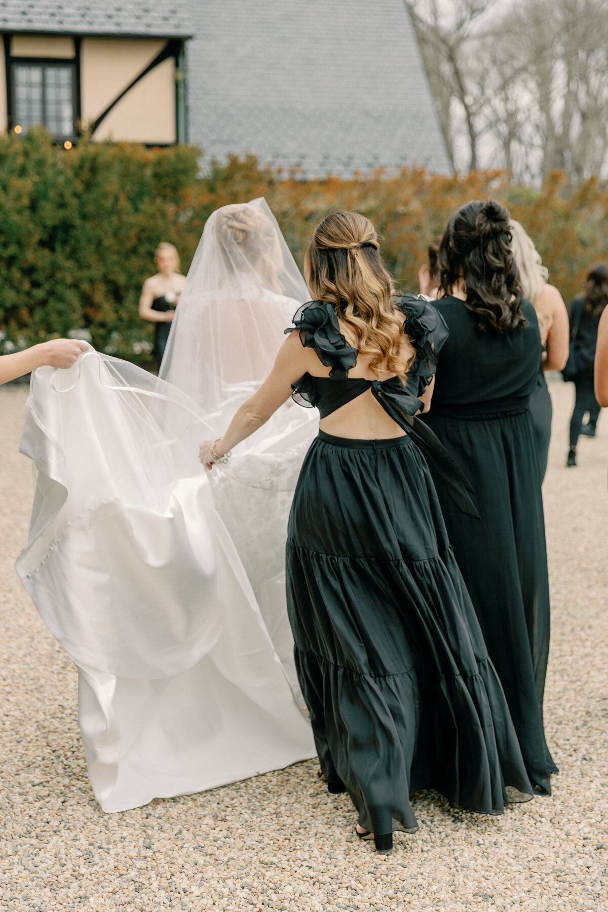 Dover Hall Estate Wedding in Richmond, VA | Wedding Photographer in Richmond | bridesmaids in black dresses helping hold the train of bride in wedding dress as she walks outside of Dover Hall in Richmond