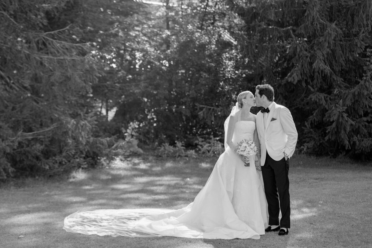 Black and white photo of the bride and groom sharing a kiss under a tree. 