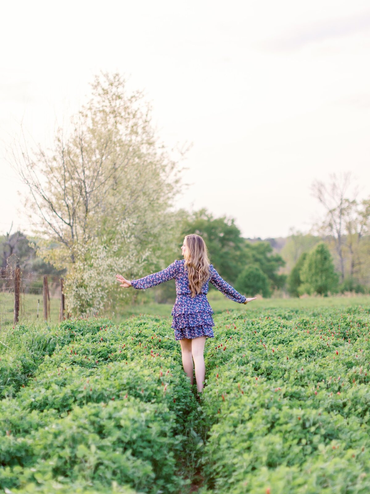 teenage girl walking through clover field with her hands help up embracing the spring day