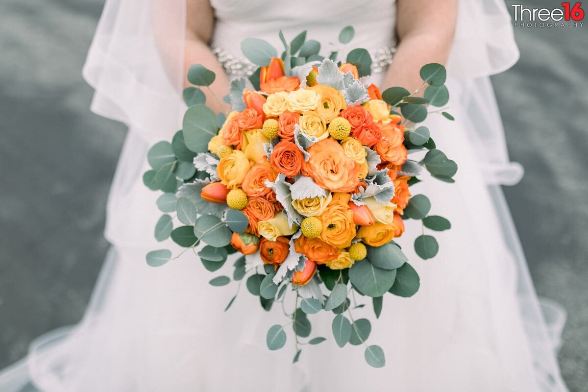 Beautiful bouquet of orange, yellow and white flowers being held by the Bride