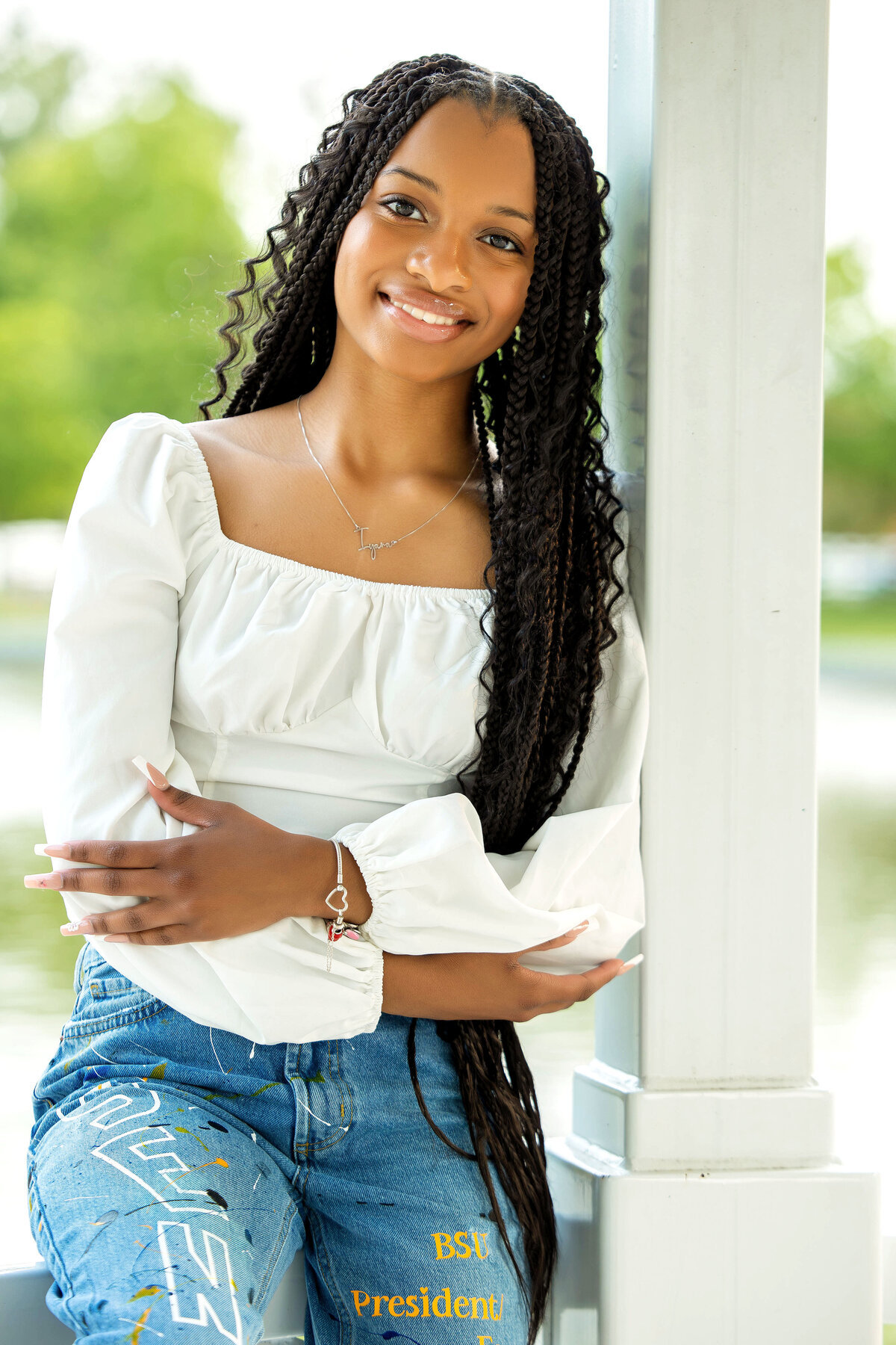 African American senior girl wearing a white princess sleeve blouse, decoratded blue jeans, and gray and whie Nikes posing in a gazebo