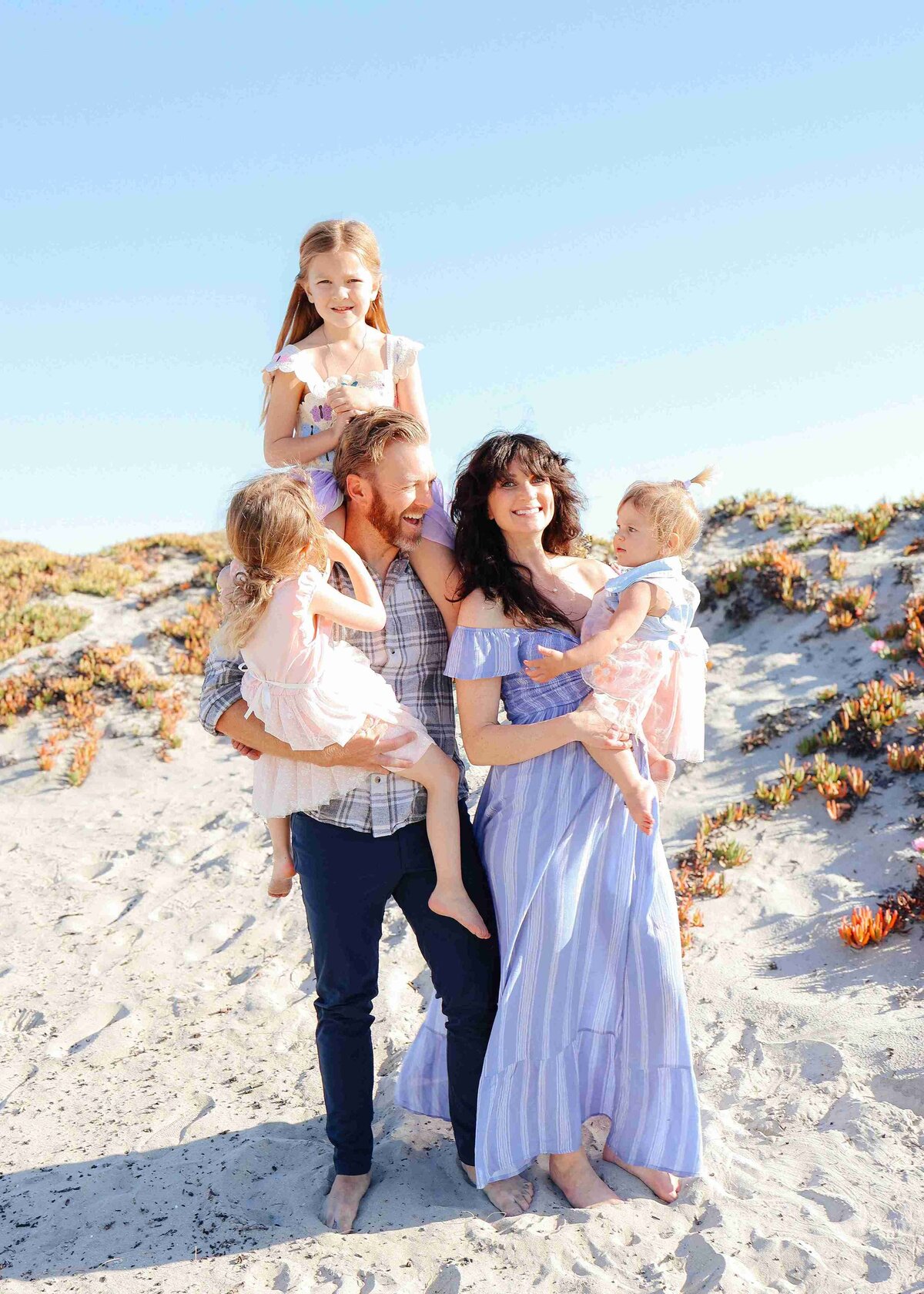 A family smiles together for a photo on the beach, captured by a family photographer.