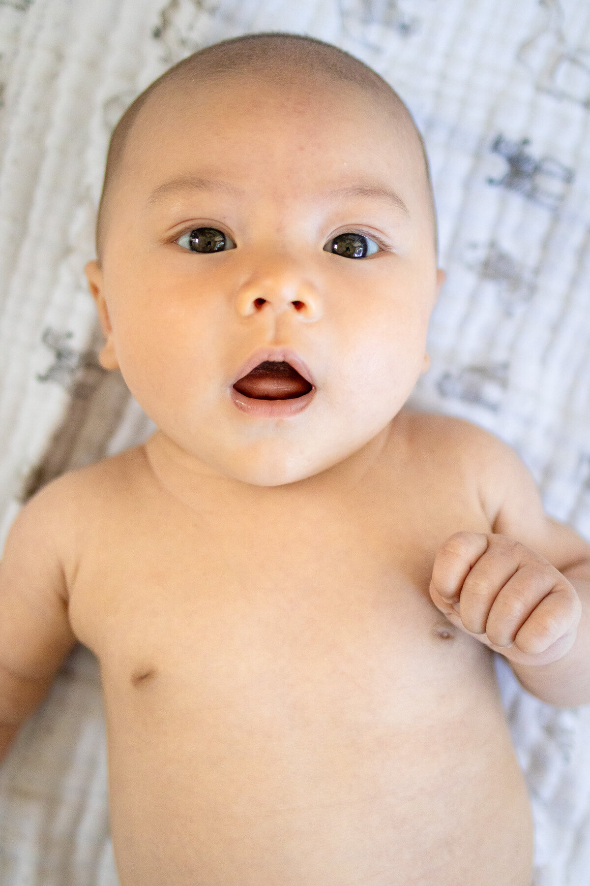 Close-up of a baby lying on a soft white blanket, mouth slightly open in curiosity – captured by San Francisco newborn photographer.