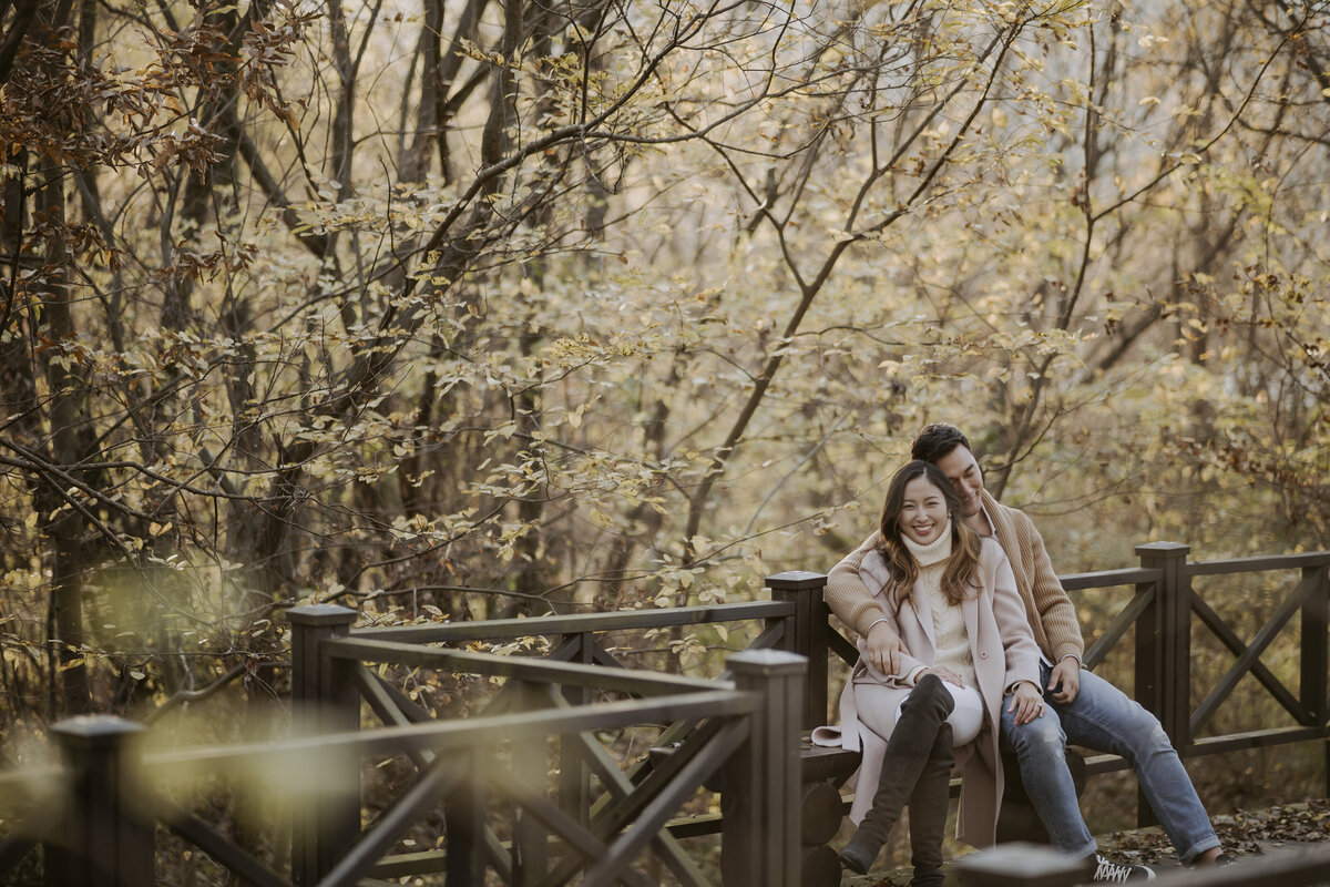 the couple sitting on the bench of the eco park in damyang surrounding with autumn leaves