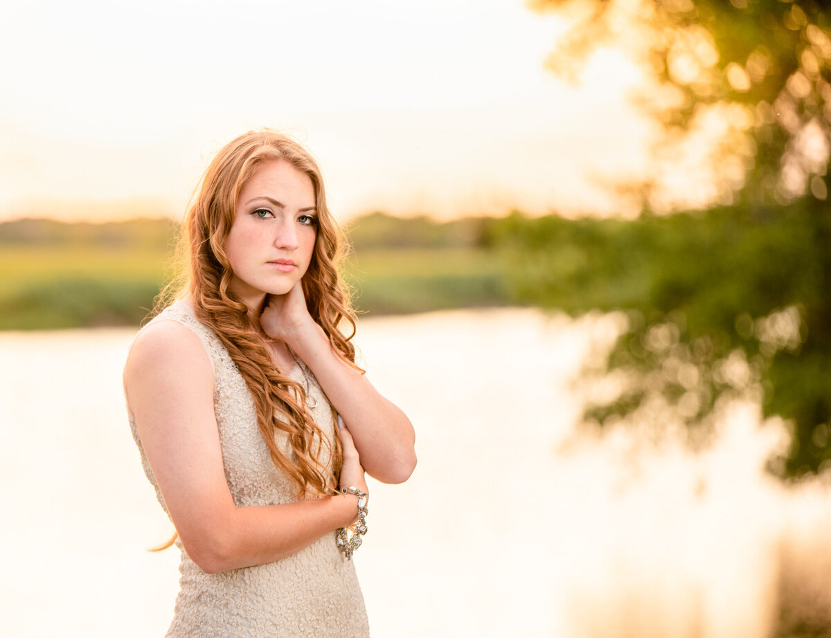 A senior girl stands in front of a creek at sunset.