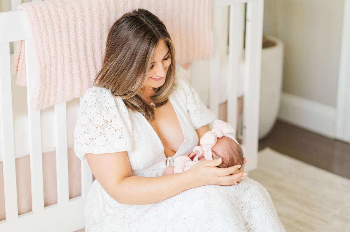 Newborn with mom sitting in front of crib looking down at her taken in Douglas, MA by the best newborn photographer in central Massachsuetts