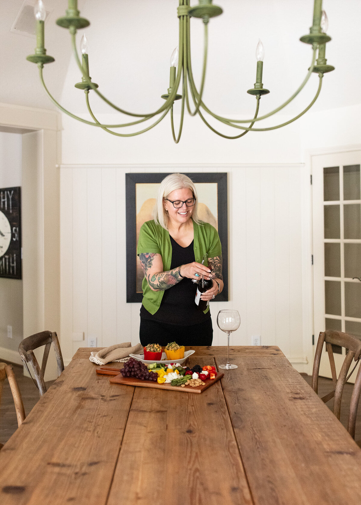 Female chef opens a bottle of wine at farmhouse table during her Oregon branding photoshoot. 