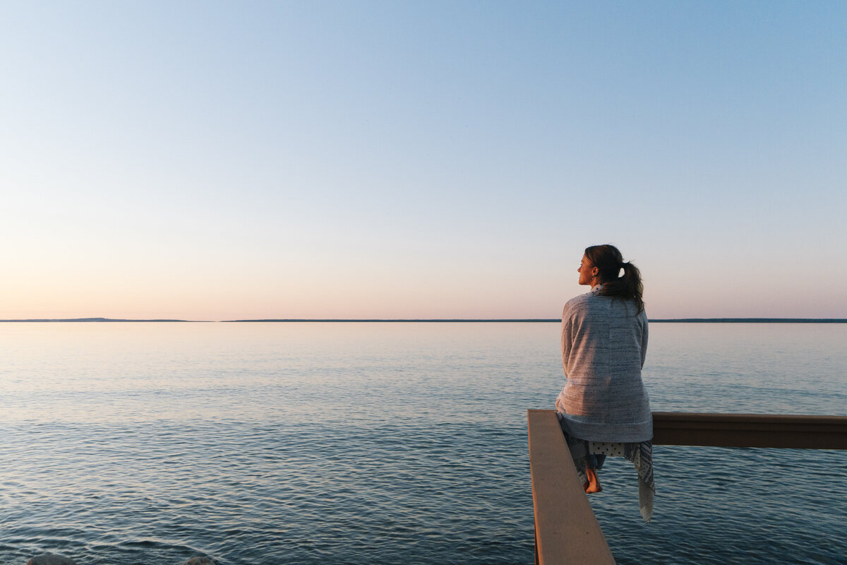 Frau sitzt auf einem Balken am Meer und sieht optimistisch in die Zukunft.