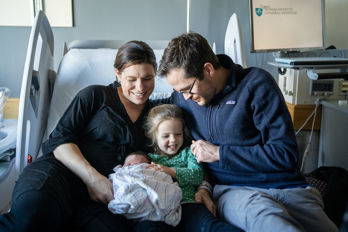 New family of four snuggling new baby on hospital bed