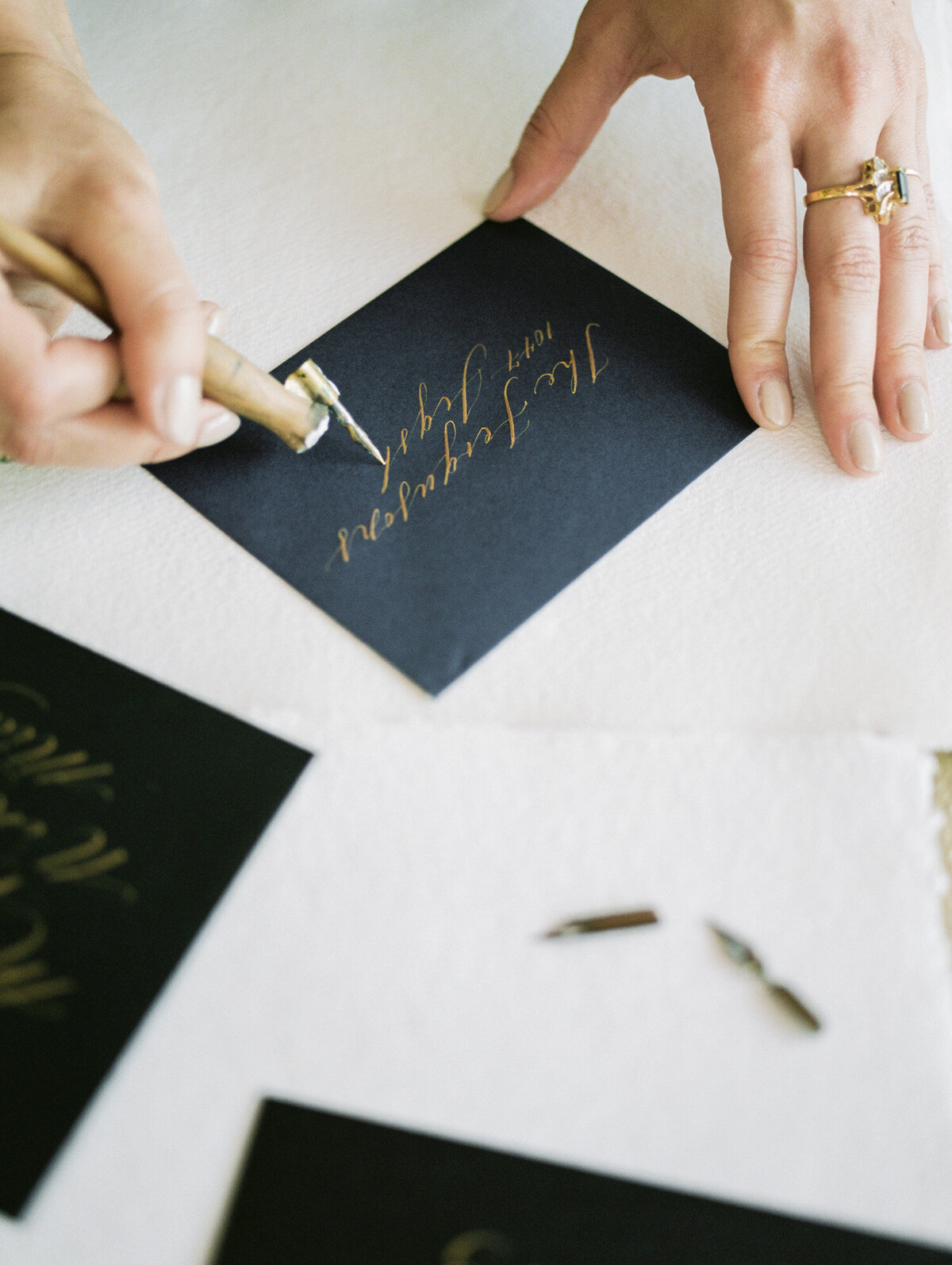 woman business owner, stationer hands with gold rings, gold ink calligraphy, black envelope