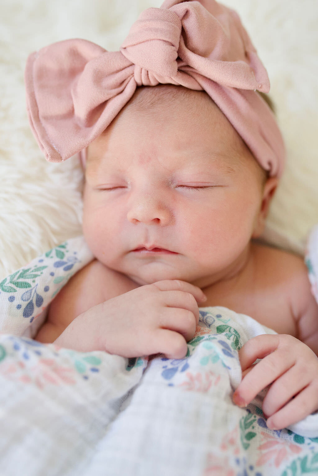 A newborn with a pink bow on sleeping soundly.