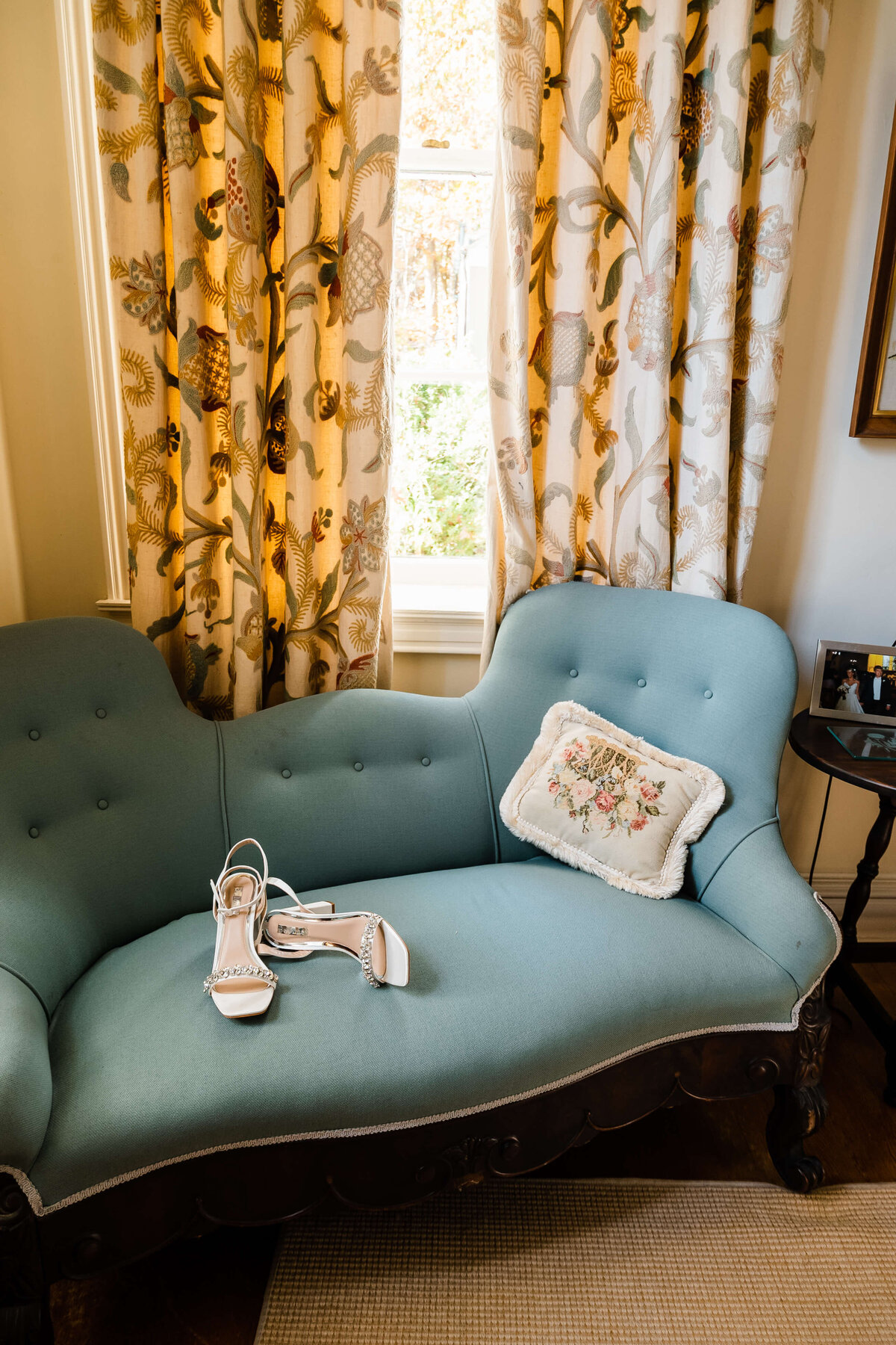 Virginia wedding photographer styles bridal suite with brides shows on a blue couch that is in front of a window that is shining in light