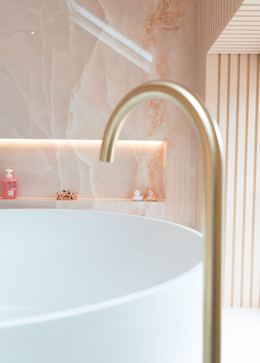 A close-up view of a round white bathtub, featuring a sleek gold faucet in a modern pink marble bathroom.