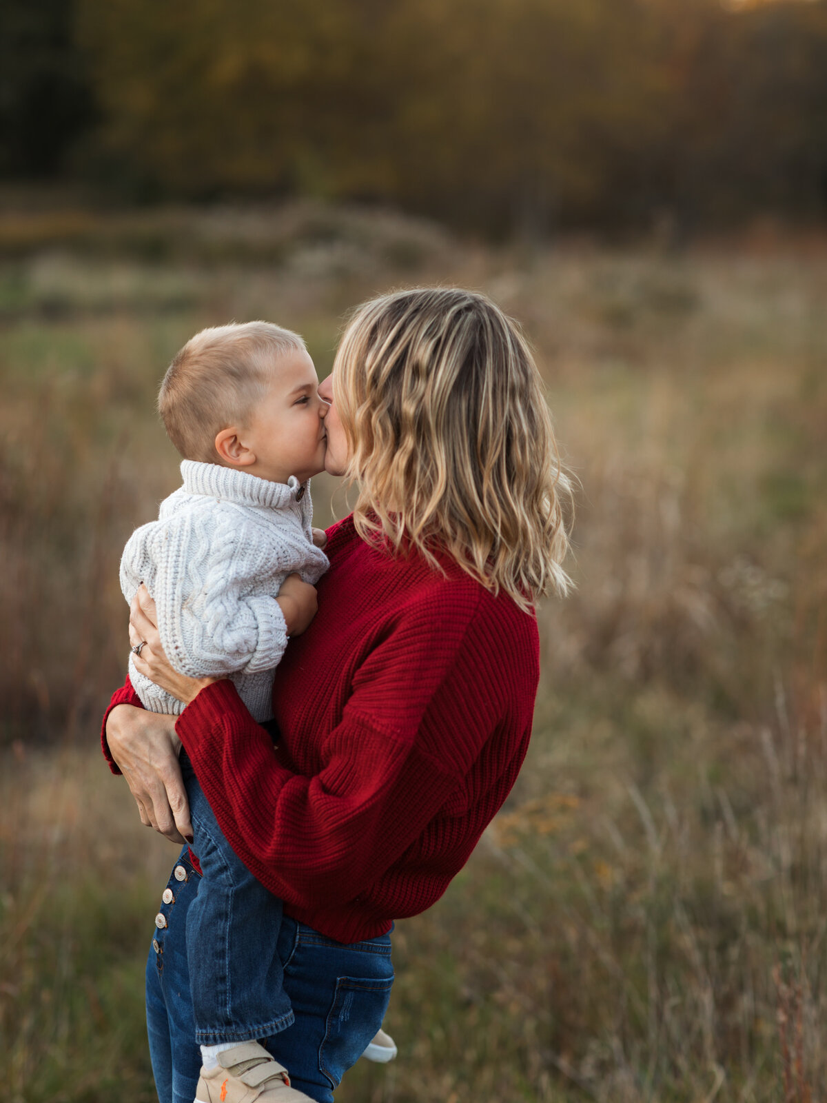mom kissing son for family photos in field