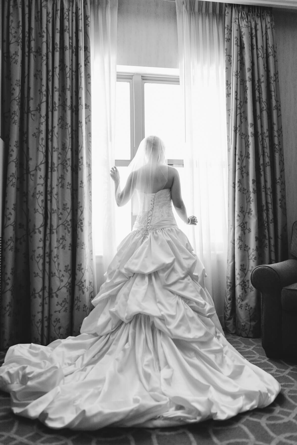 A bride looks out the window as her dress flows behind her.