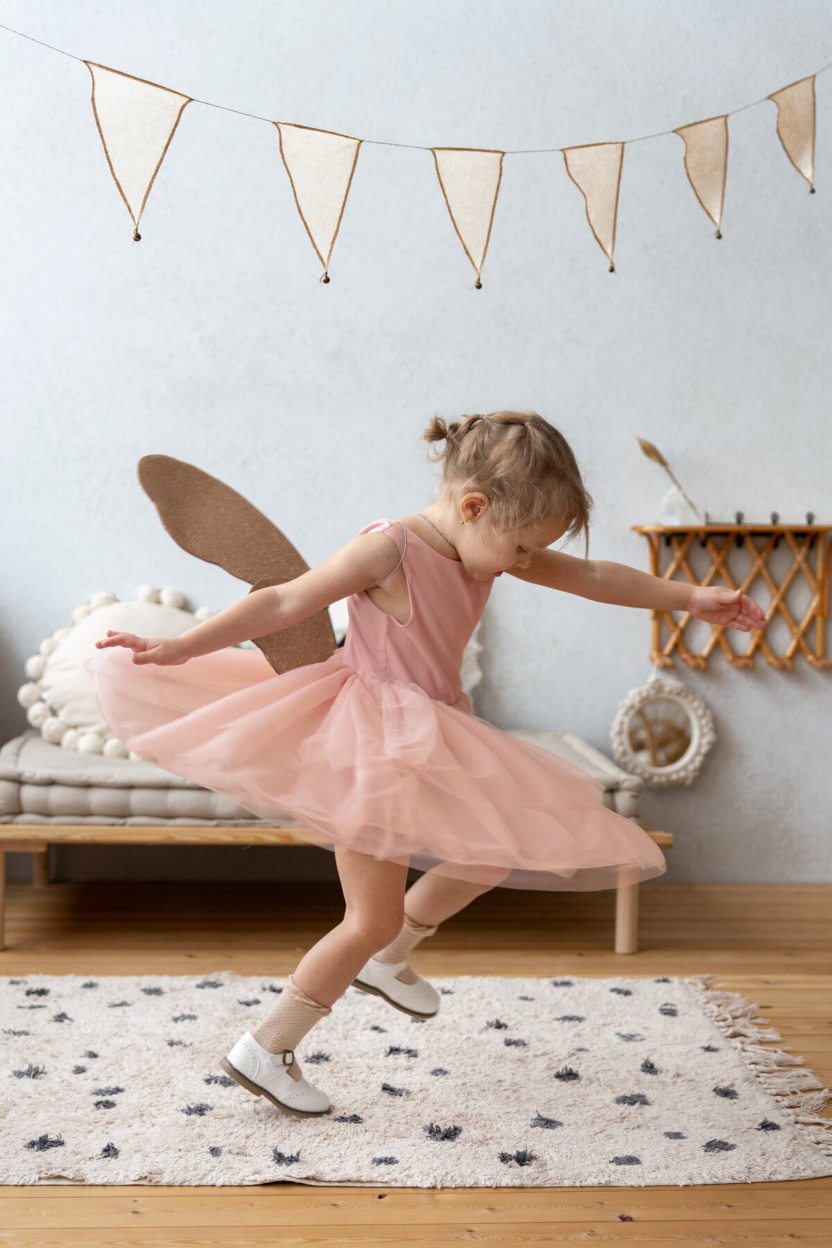 Petite fille en tutu rose, ailes en carton dans le dos, tournoyant dans sa chambre.