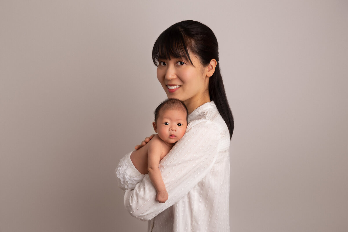 Mother smiling and holding her newborn baby who is leaning on her shoulder.