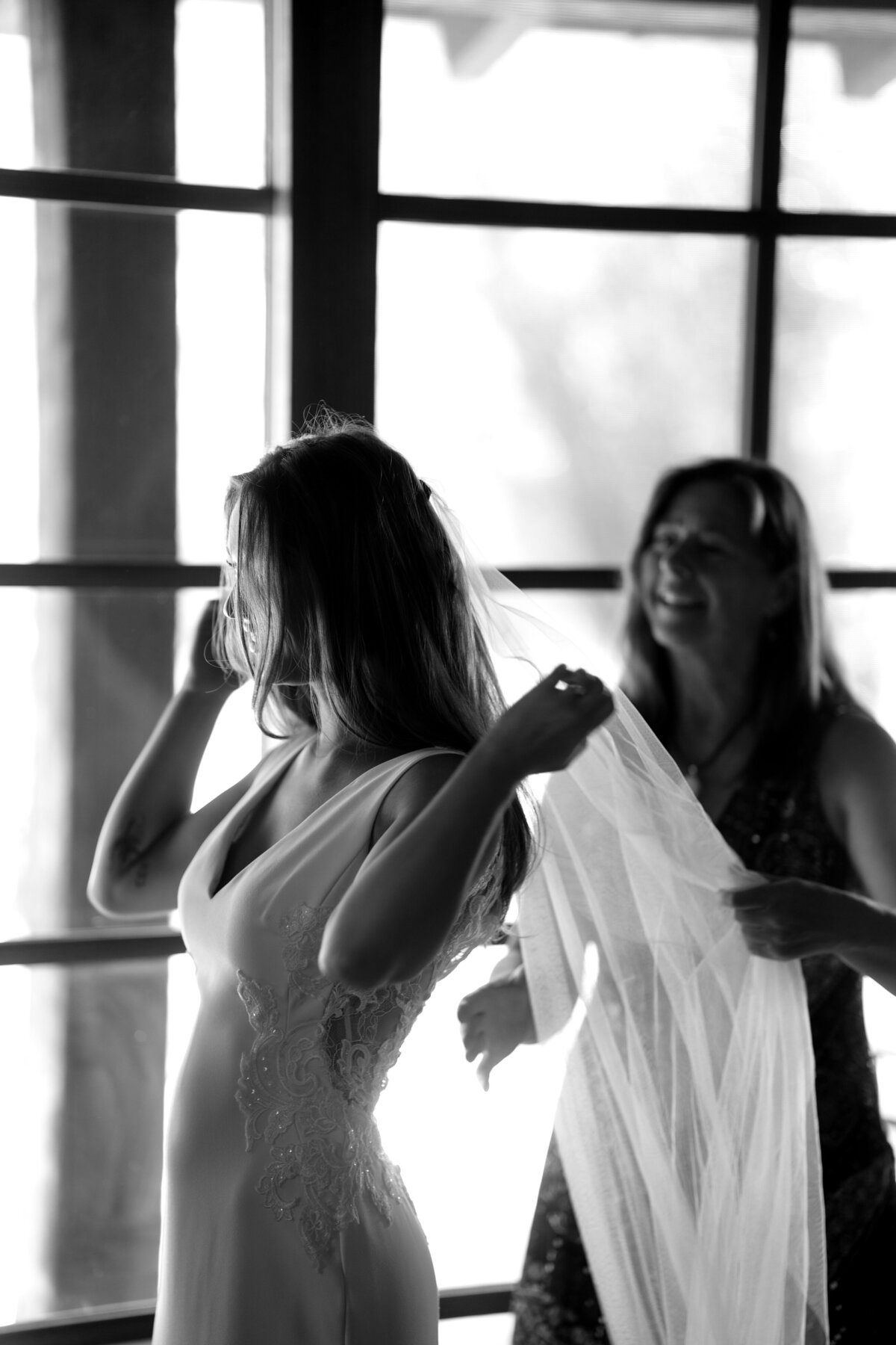 A bride and her mother putting her veil together, smiling at each other.