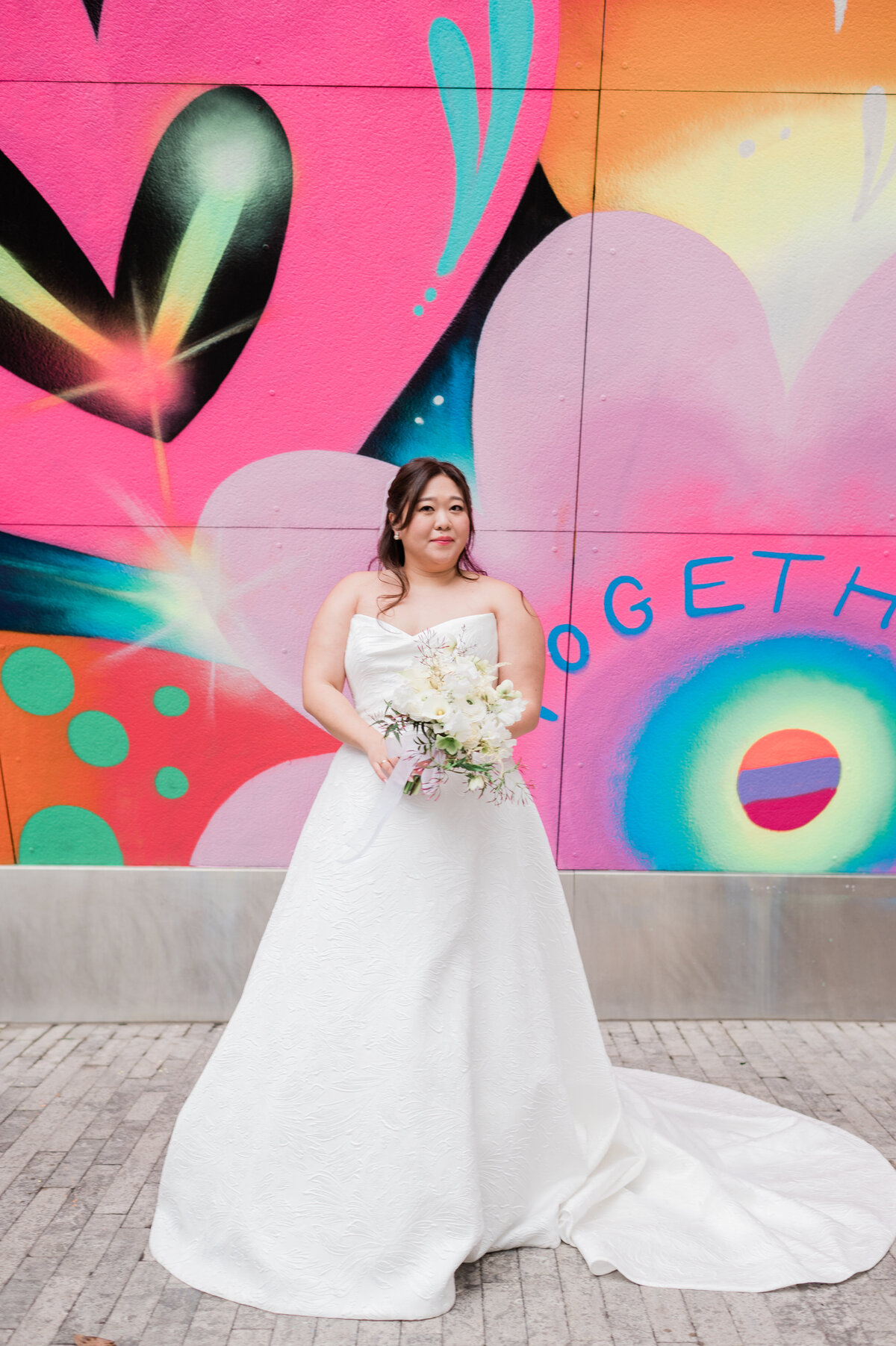 Bride stands in front of NYC mural smiling with her bouquet in hand