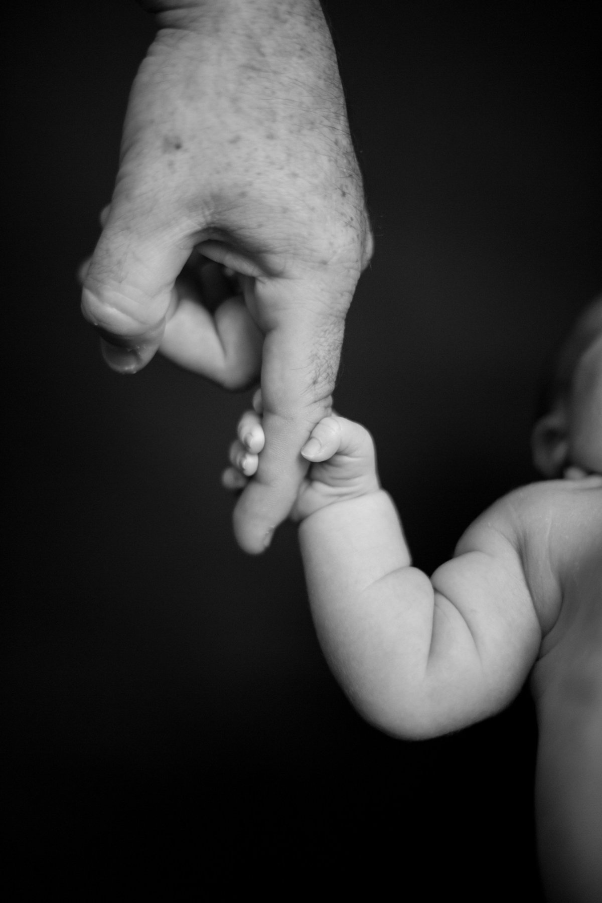 Black and white photo of newborn baby holding fathers finger.