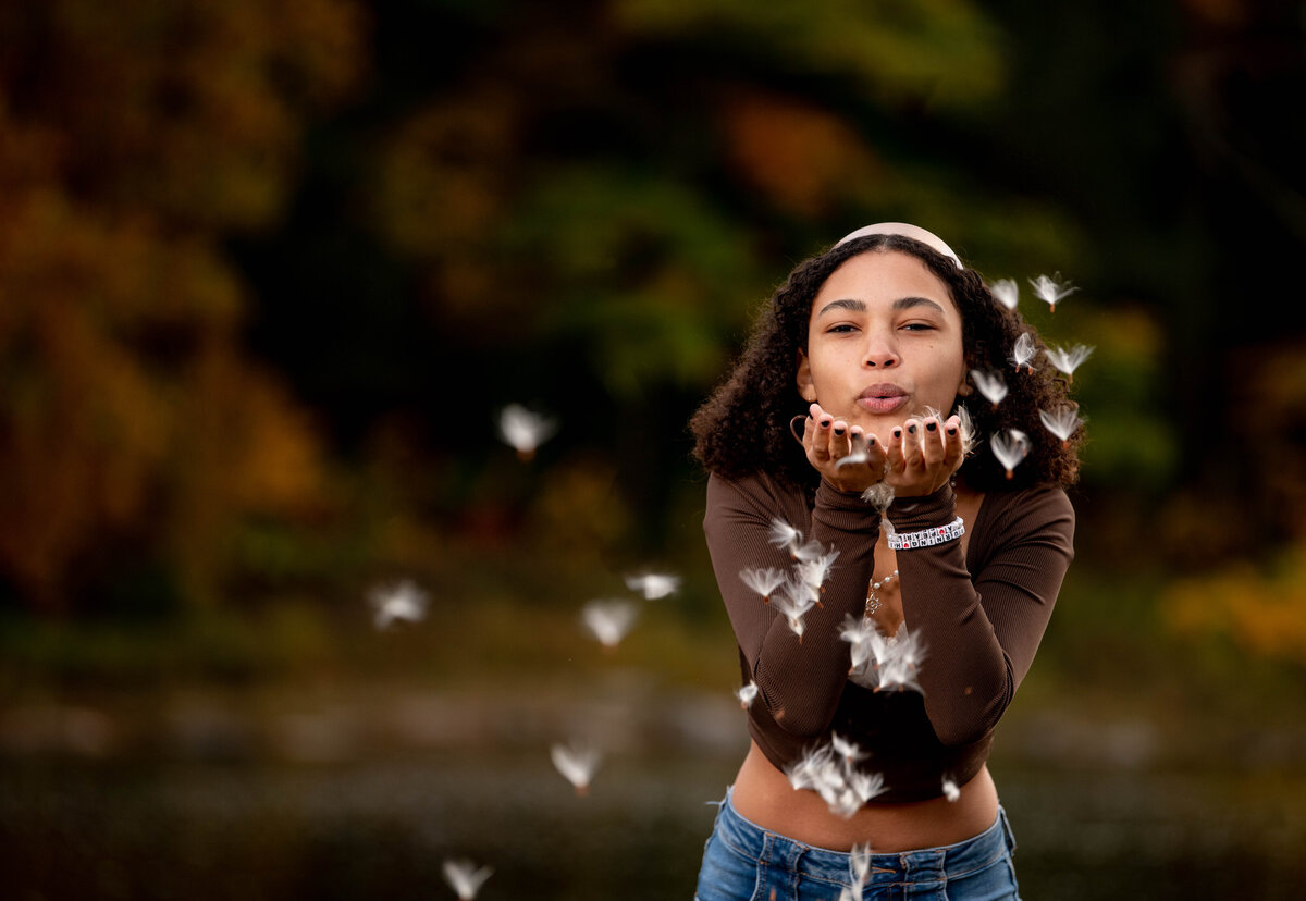 a high school senior blows milkweed out of her hands in front of the delaware river in callicoon