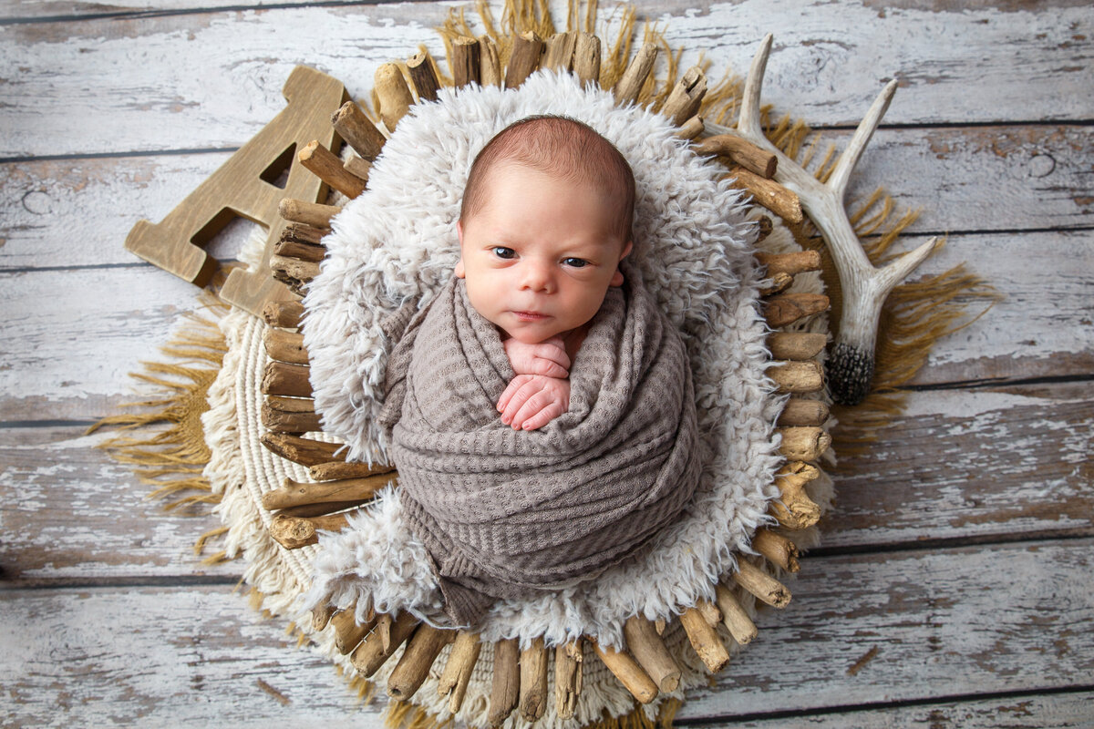 Portrait of a baby wrapped in a brown scarf and laying in a natural looking basket with boho  styling by Life in Pink Photography