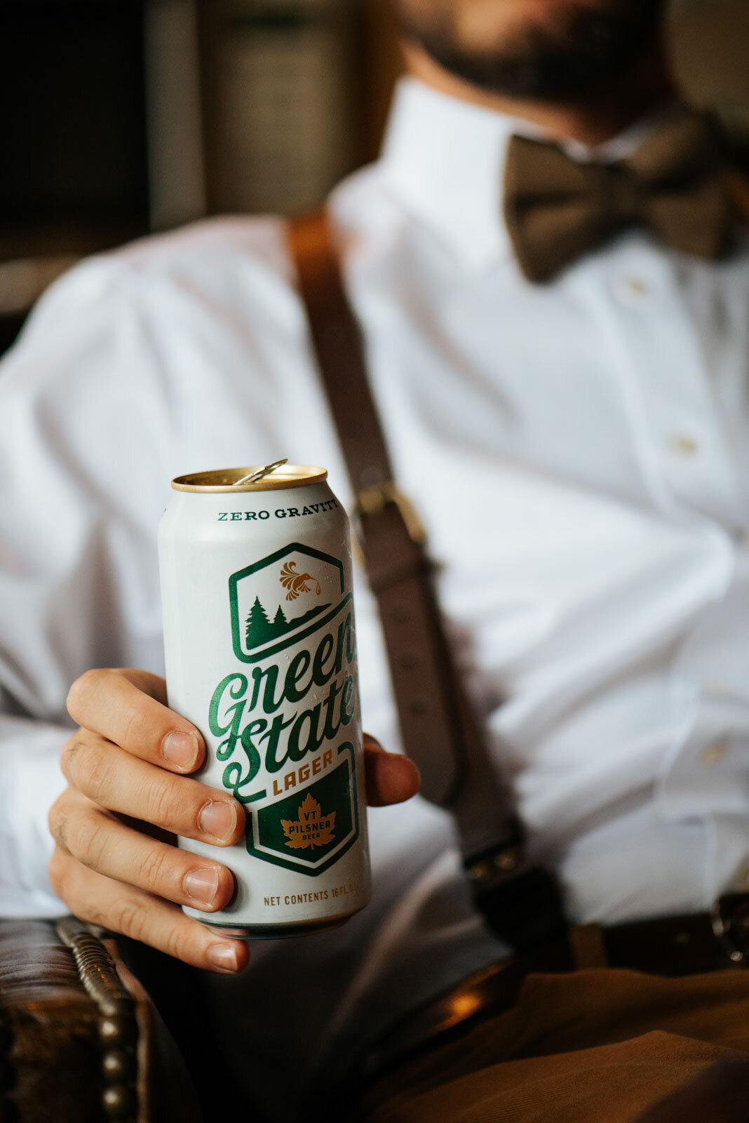 green state lager groom holding beer close up with suspenders at mountain top inn in chittenden vermont elopement