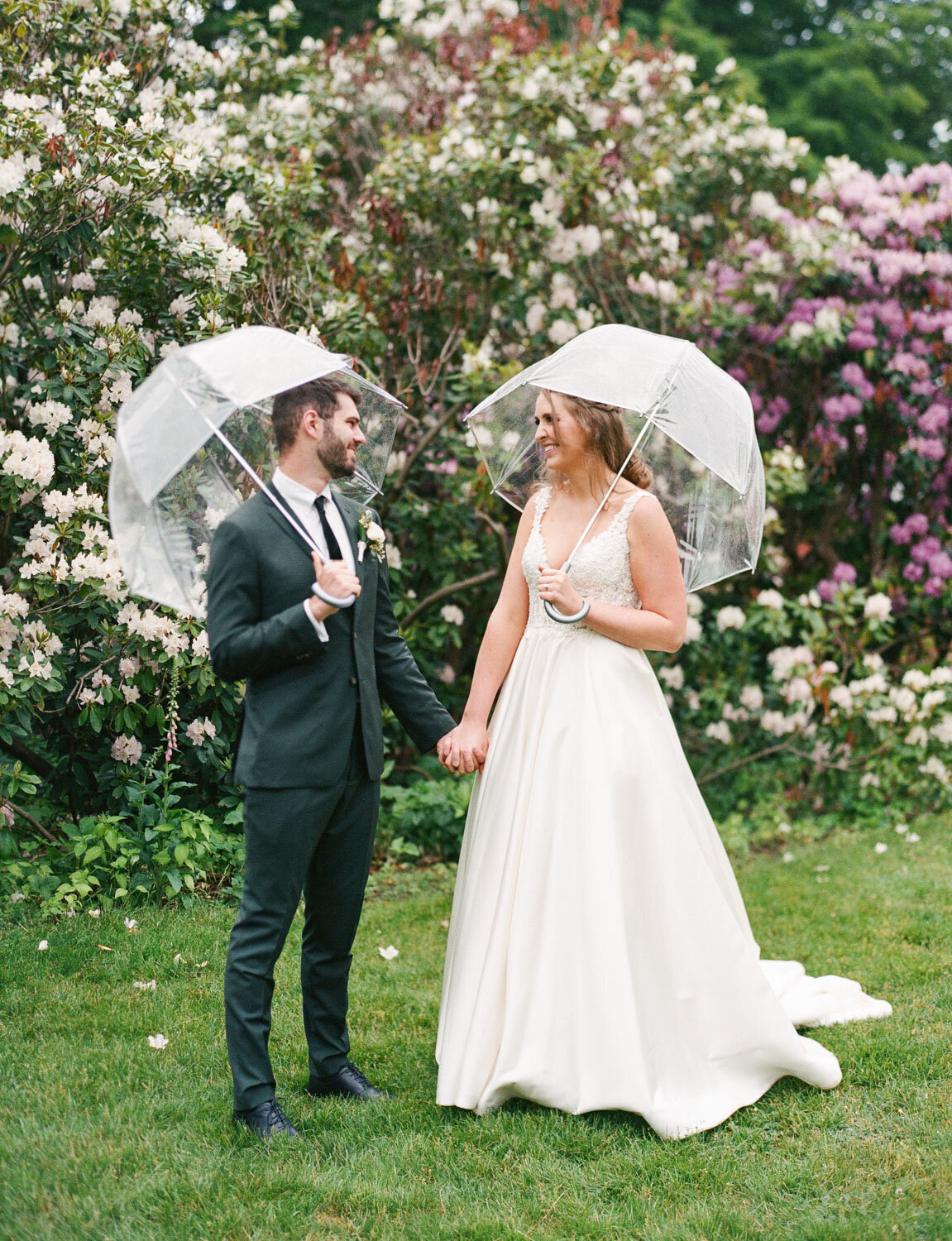 Bride and groom looking at each other smiling and both holding their clear umbrella