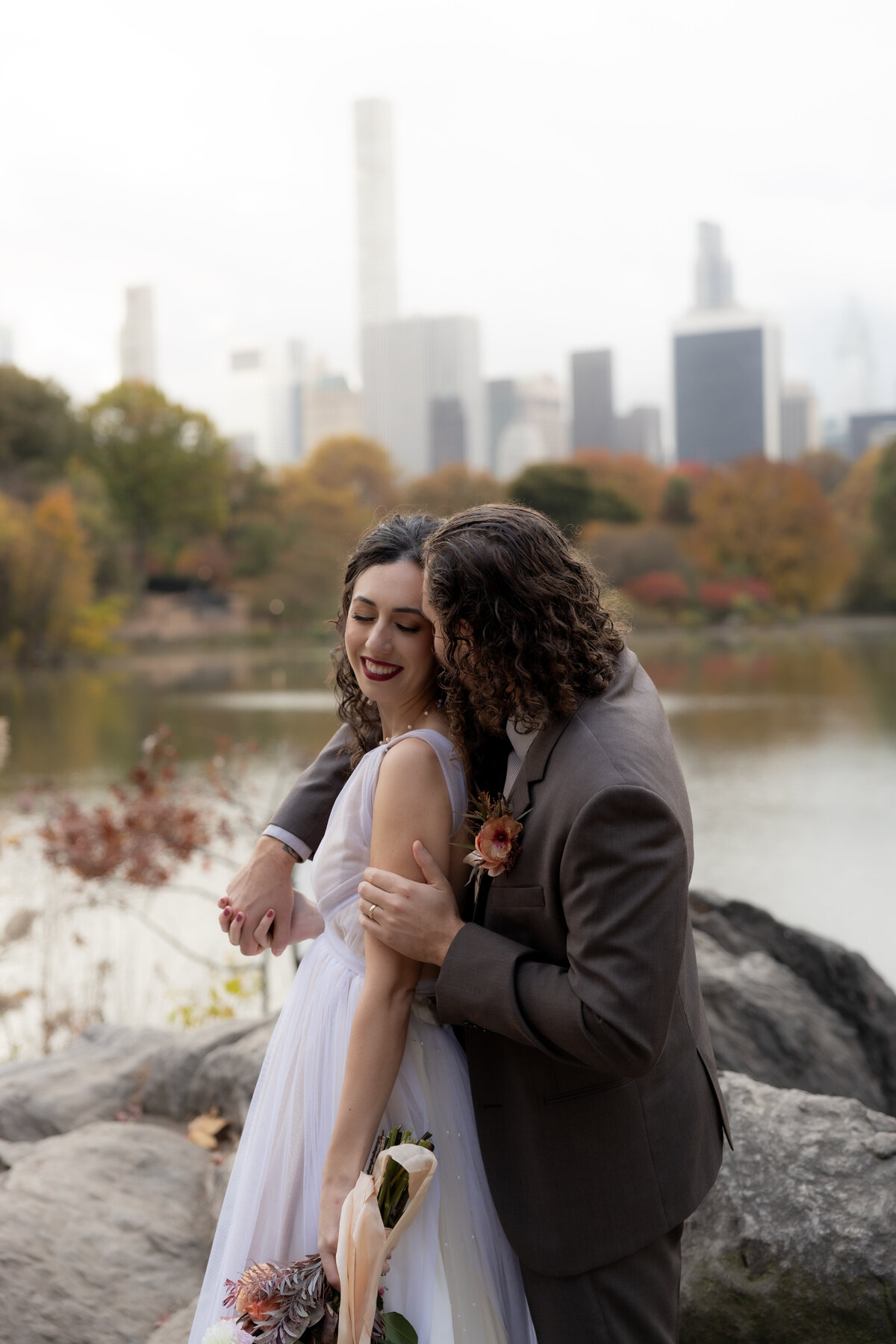 The couple holding hands and smiling as they walk through a peaceful Central Park path.