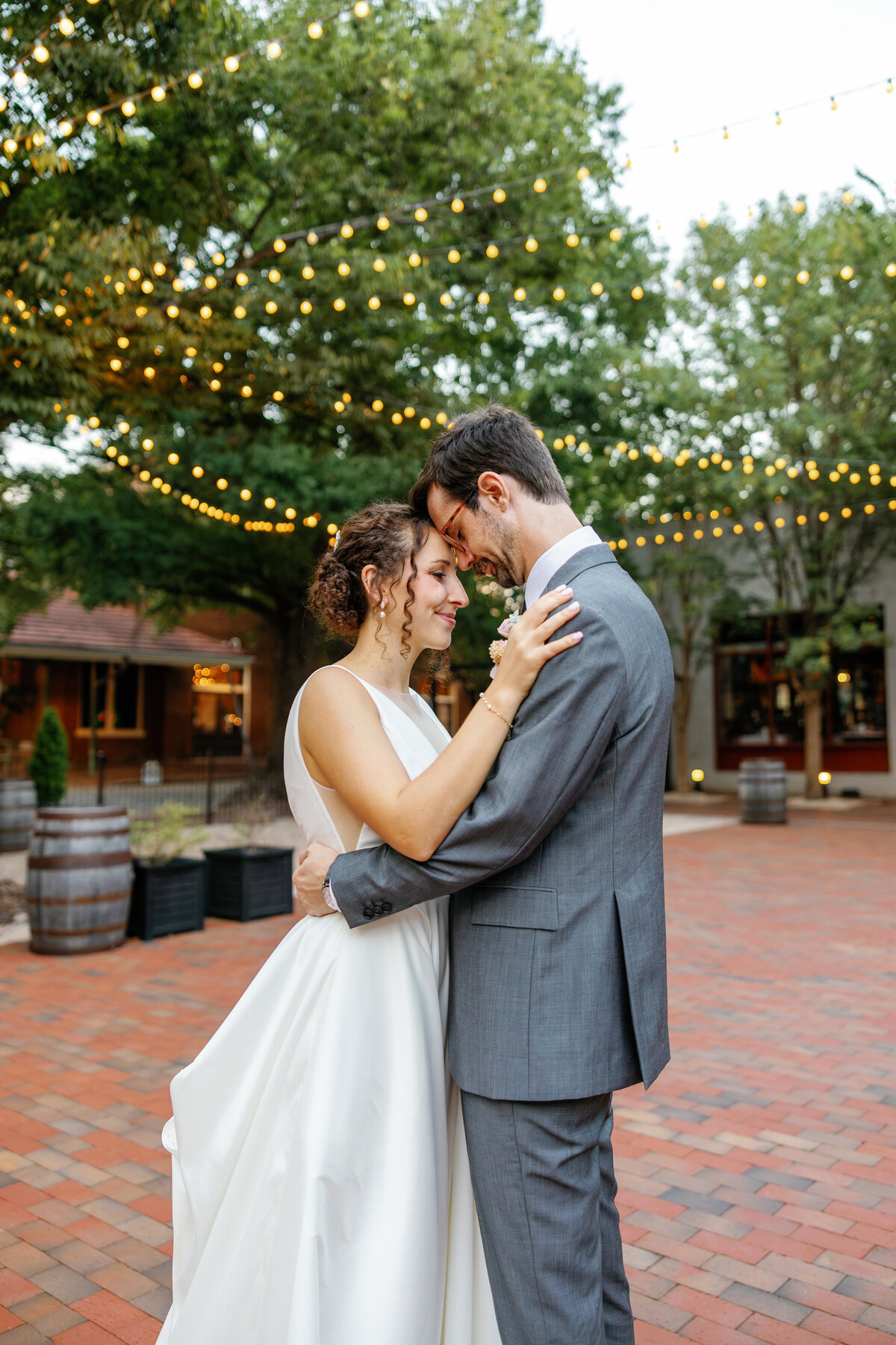 Newlyweds embracing under twinkling lights at Market Hall, intimate Raleigh wedding photo