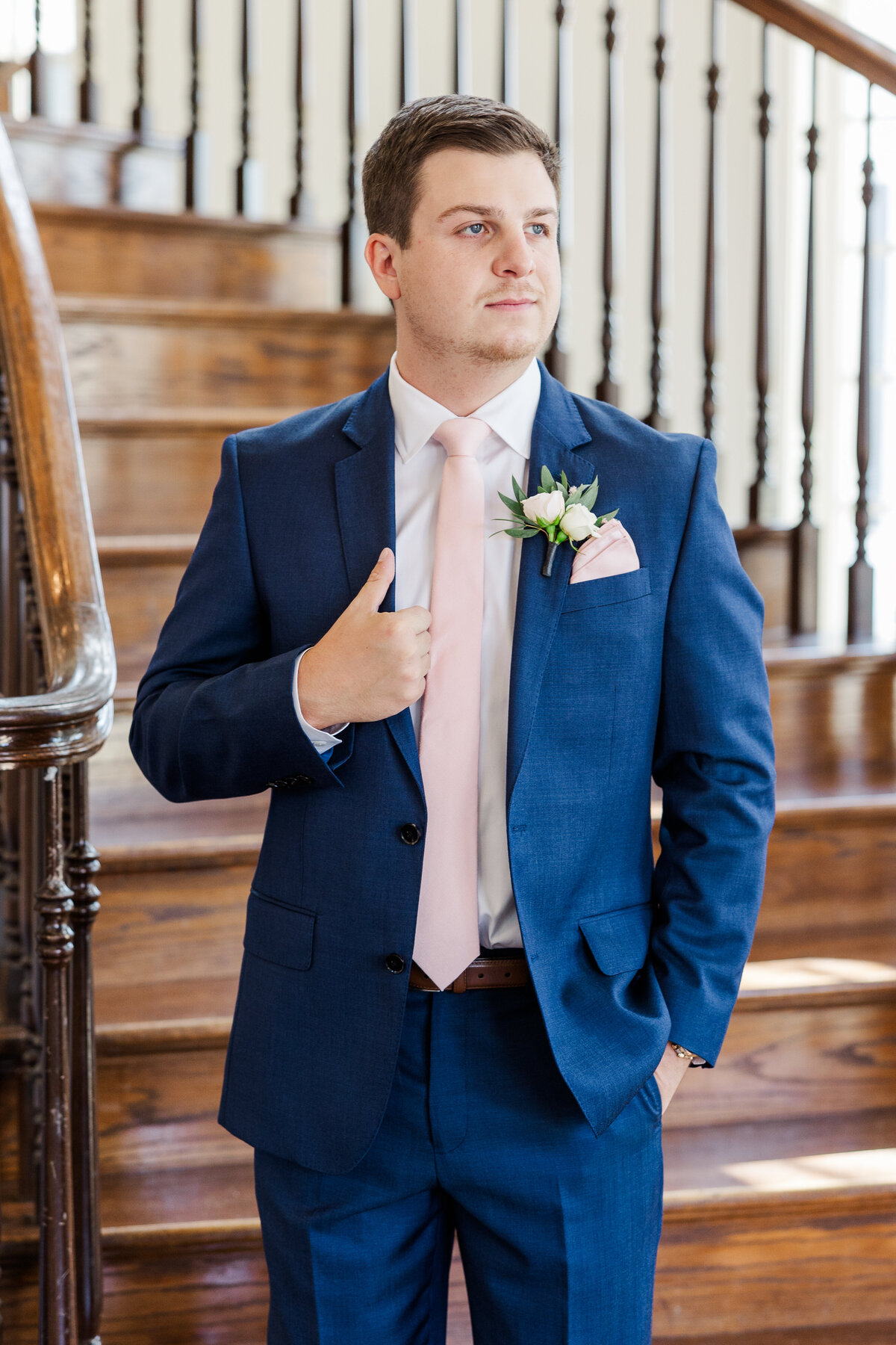 A refined groom poses in a tailored navy suit and blush tie, captured on the grand staircase of a romantic wedding venue near McKinney, Texas. A timeless and stylish portrait perfect for a modern Southern celebration.