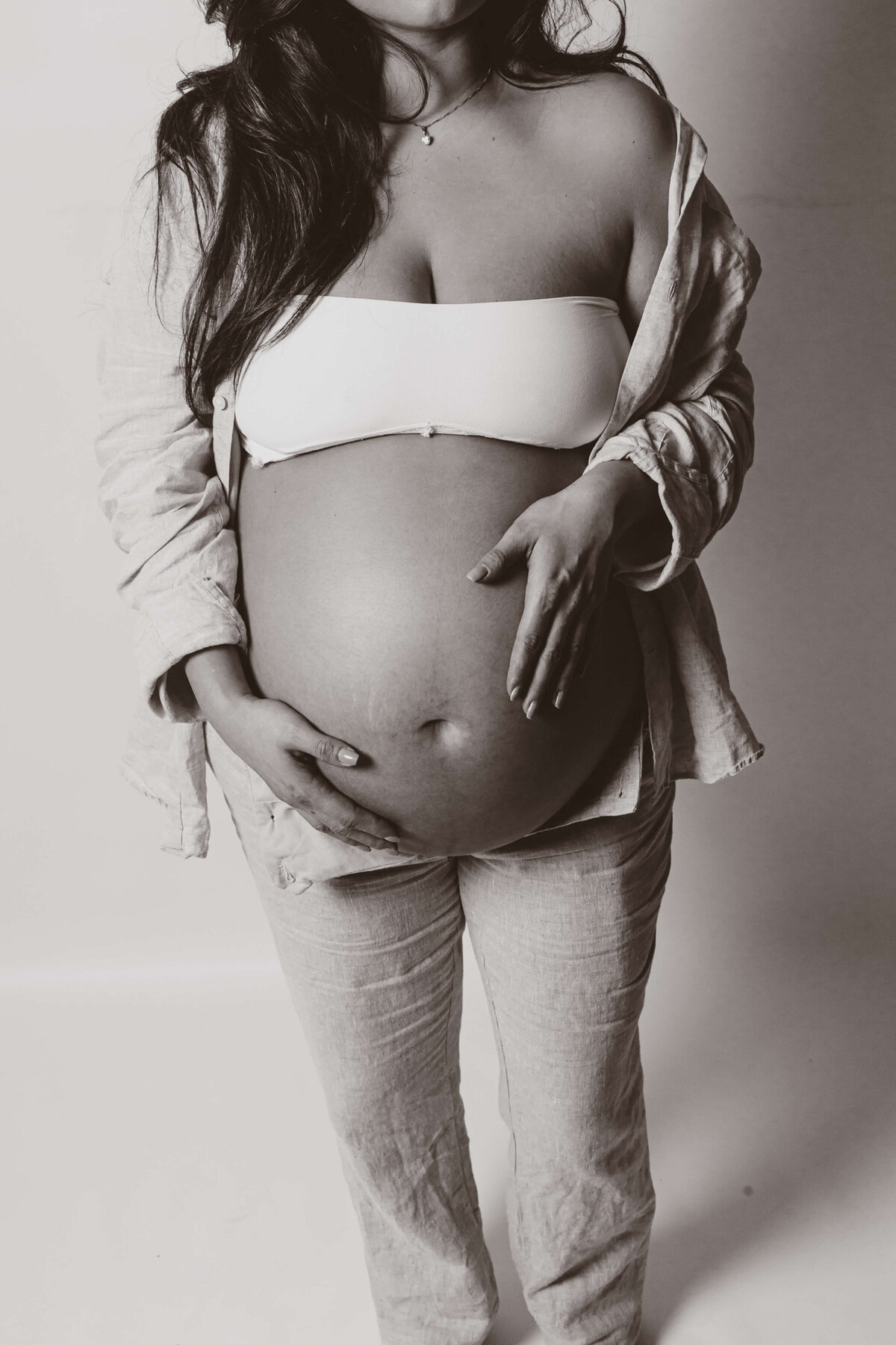 En gravid kvinna ståendes med båda hennes händer på sin gravida mage under en gravidfotografering i studio Stockholm