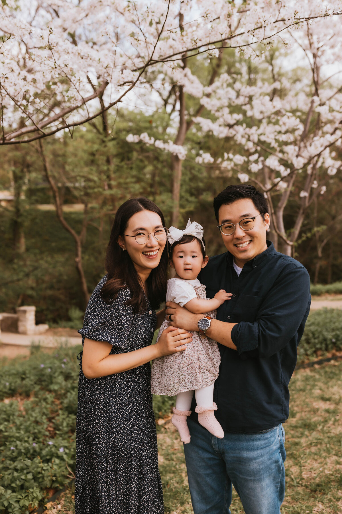 cute asian family of three smiling in the cherry blossoms