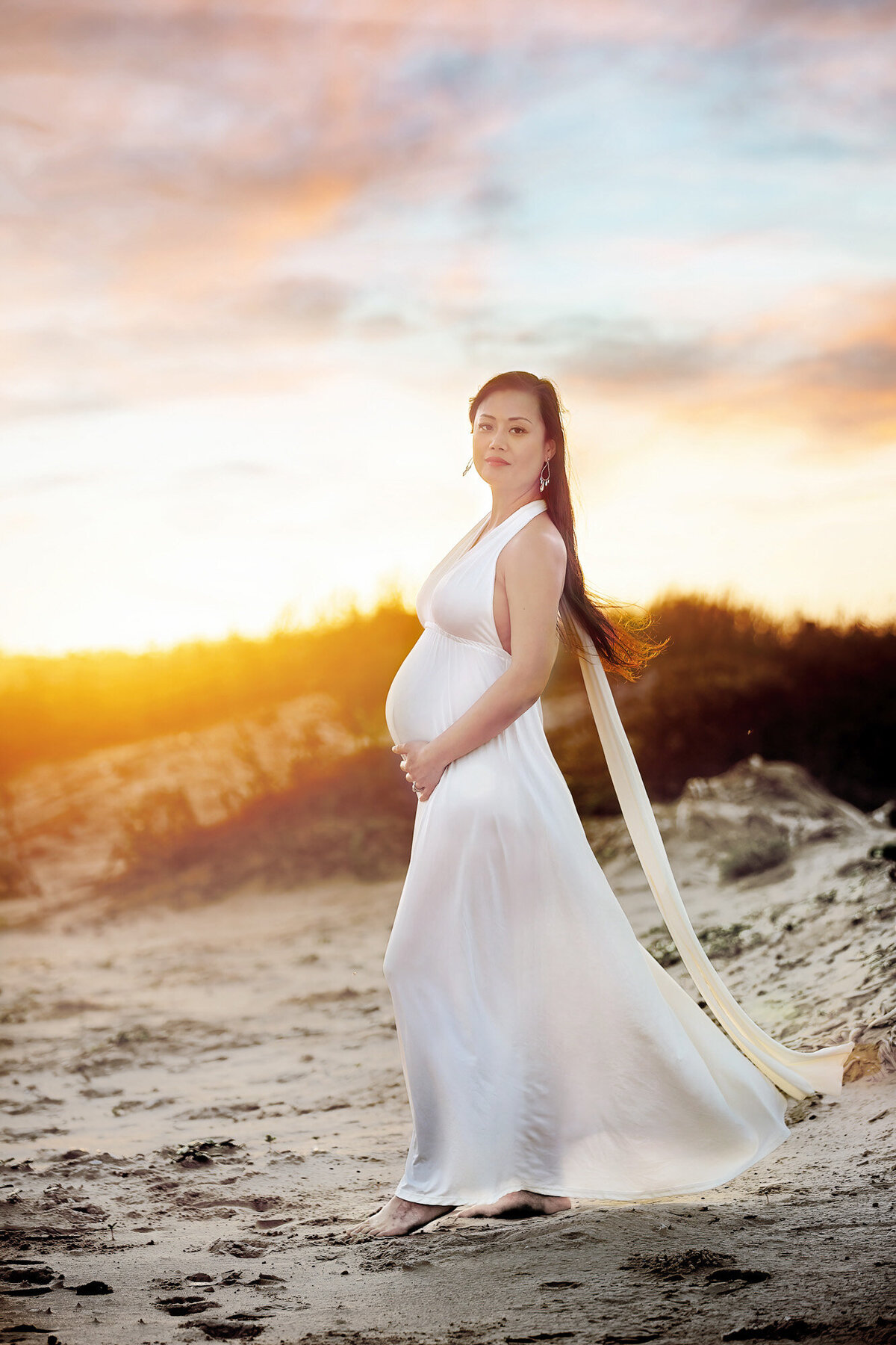 Beautiful maternity model wearing a long white dress at the beach