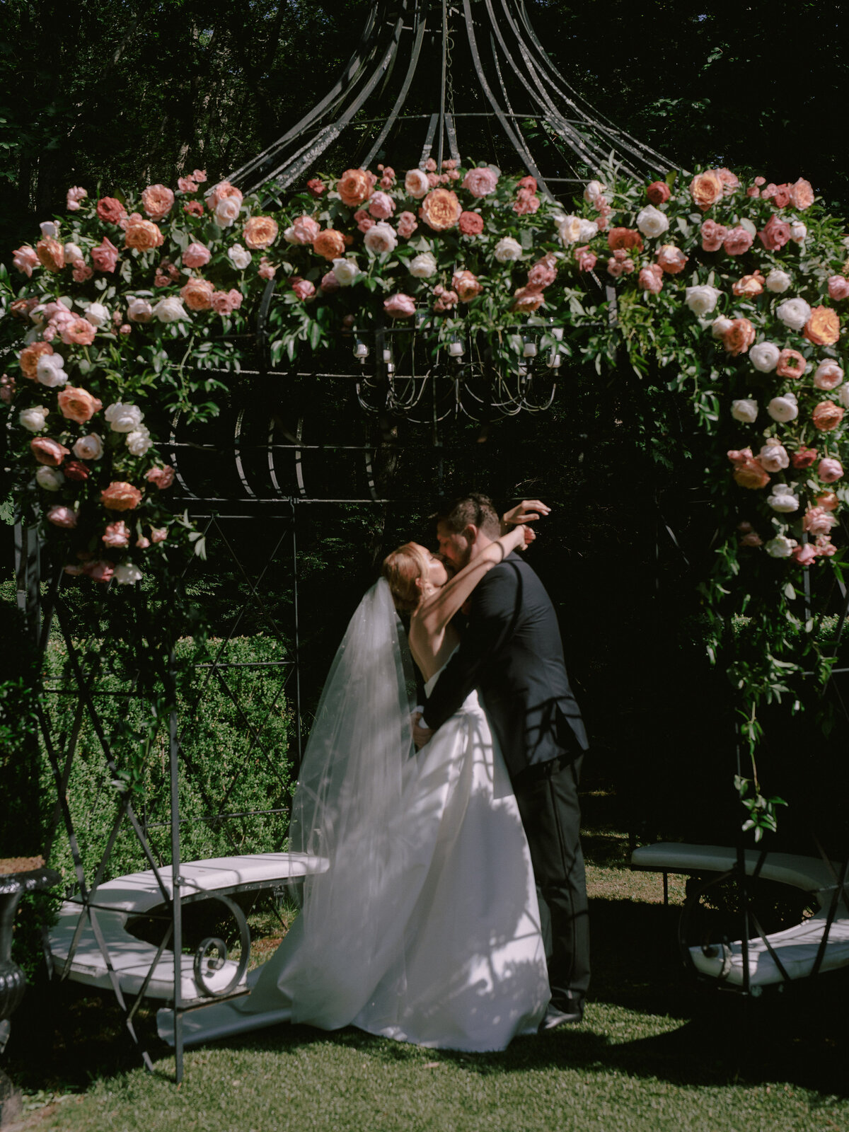 A couple kisses under a floral arch at their Lord Thompson Manor wedding