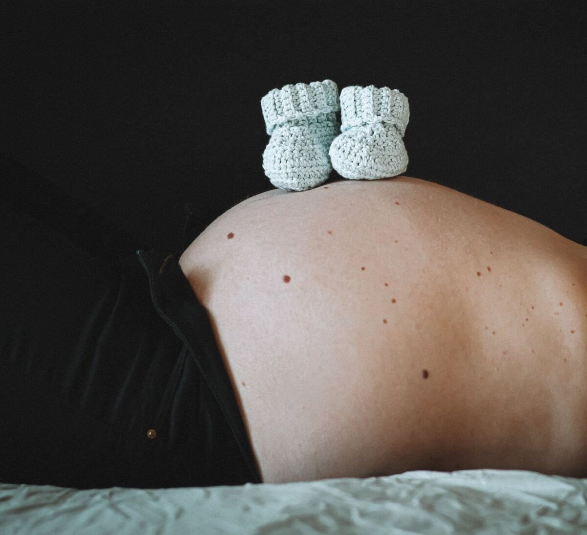 Een zwangere buik met een paar schattige, gebreide babyschoentjes erop, gefotografeerd in een zachte, intieme setting