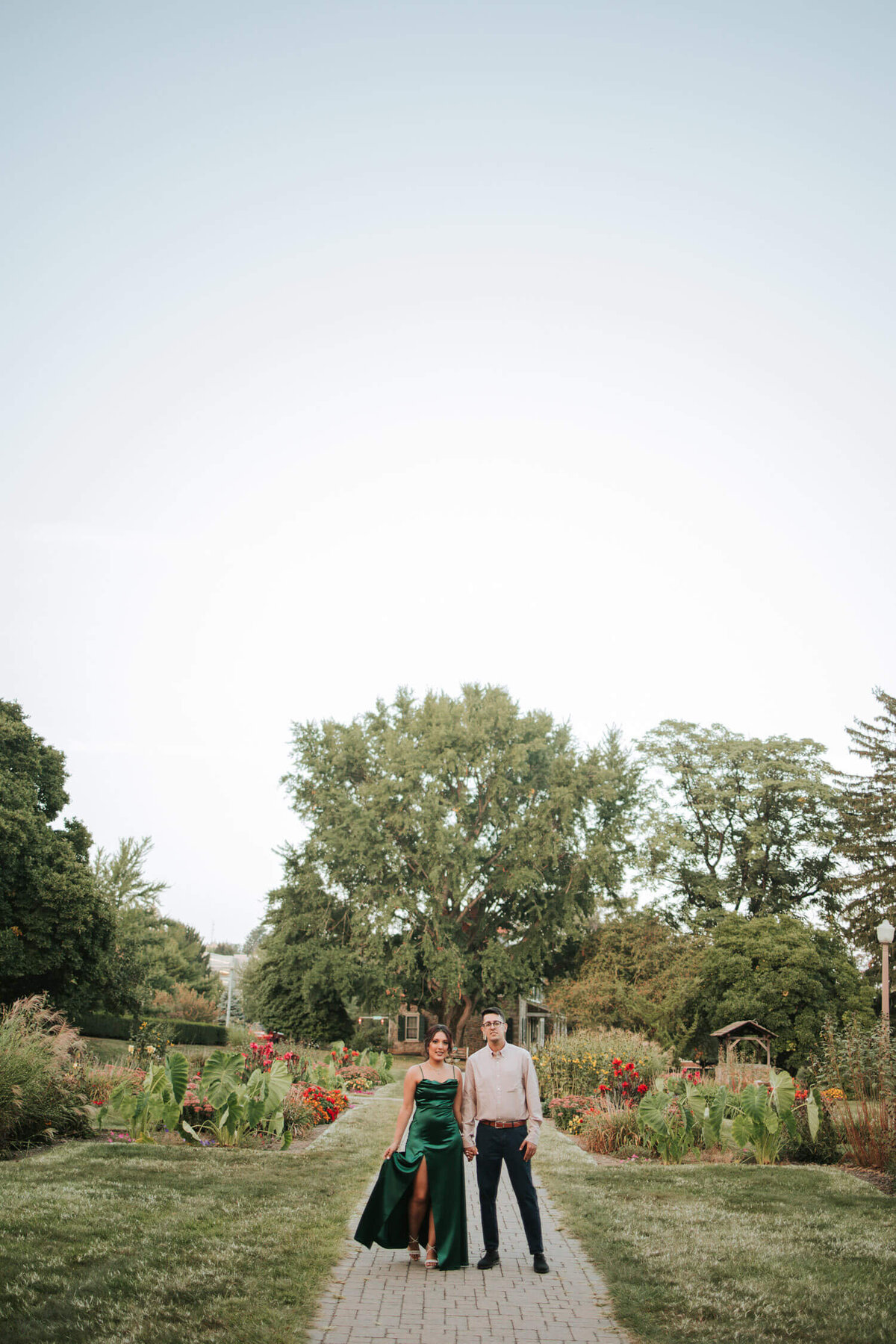A couple walks hand in hand through a lush garden during their engagement session in Rosewood Garden in Lehigh Valley.